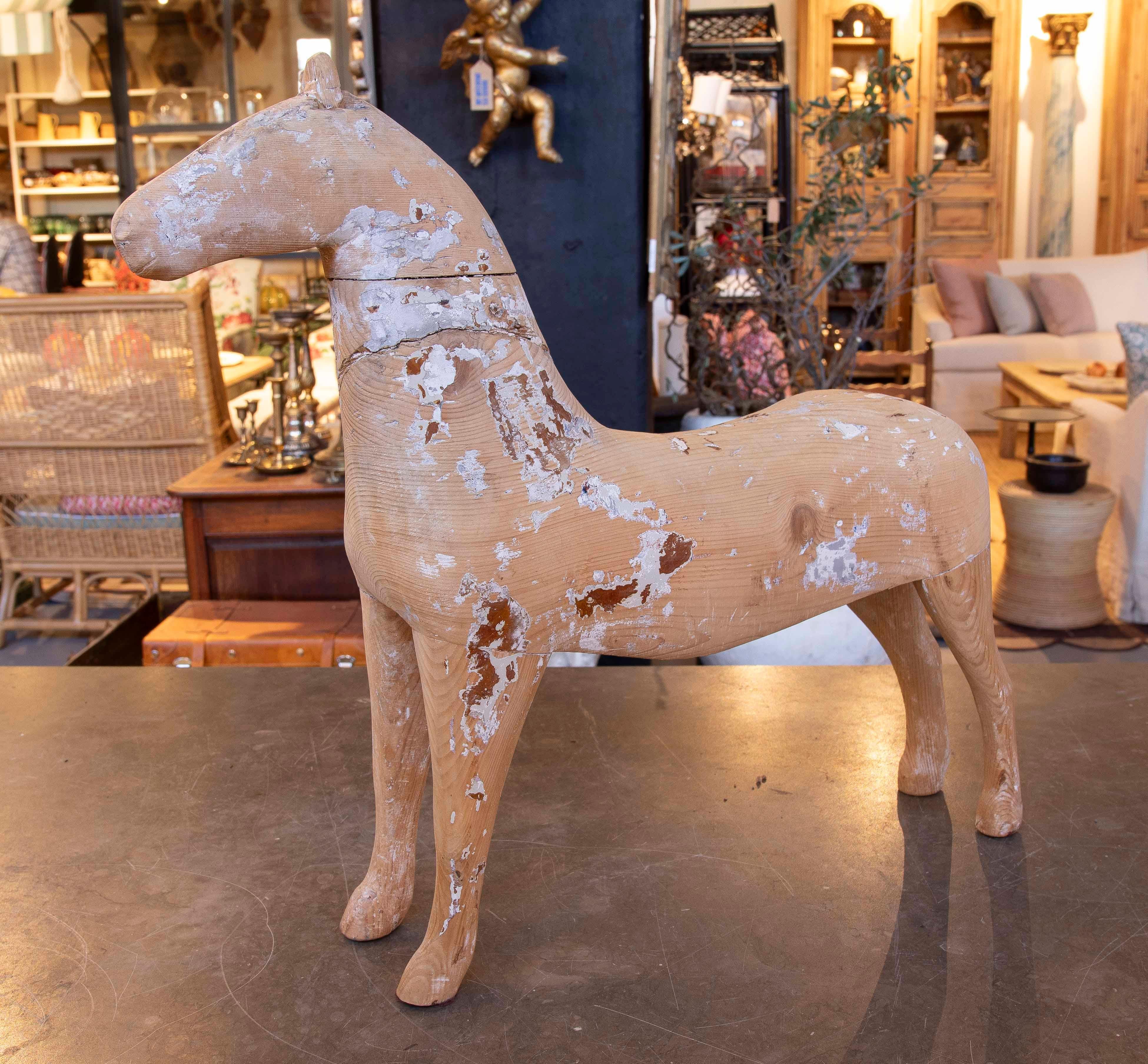 Hand-carved wooden horse figure, with worn details that reflect its character and antiquity. The finish shows a combination of natural wood and areas of faded paint, giving it a rustic and authentic charm. Perfect as a decorative element in spaces