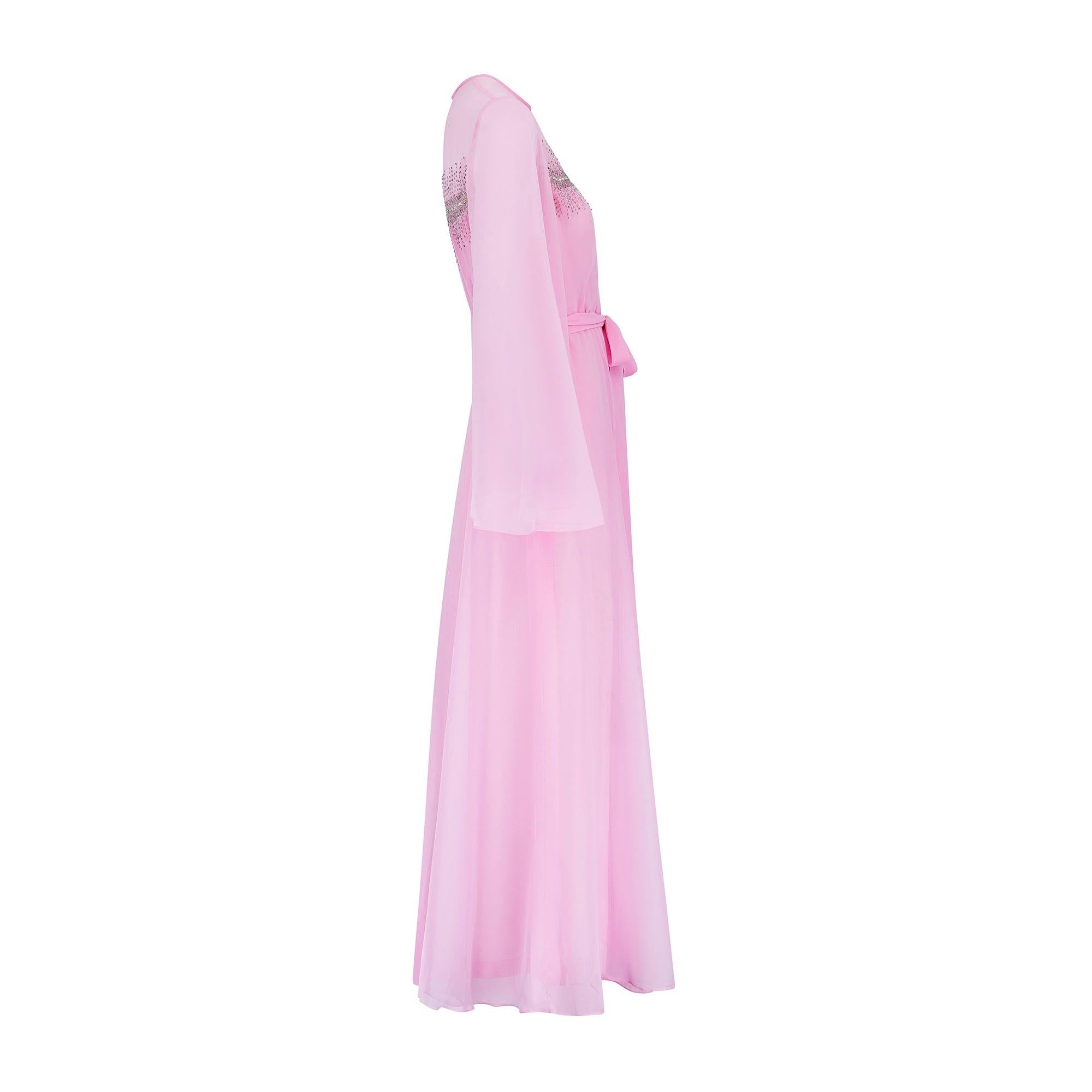 This striking evening dress by Hannalore of London combines fairy tale glamour with a  late 1960s to early 1970s silhouette. Tailored from bubble-gum pink chiffon, it has a full, swirling skirt and theatrical angel-sleeves that create wonderful