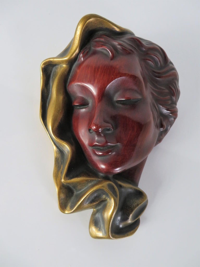 Lovely Hans Schirmer wall hanging of a beautiful woman with swirling fabric about the head, painted in a reddish brown tint and gilt the fabric. Retaining the gold foil label of the workshops of the German company Achatit Werkstätten, which was