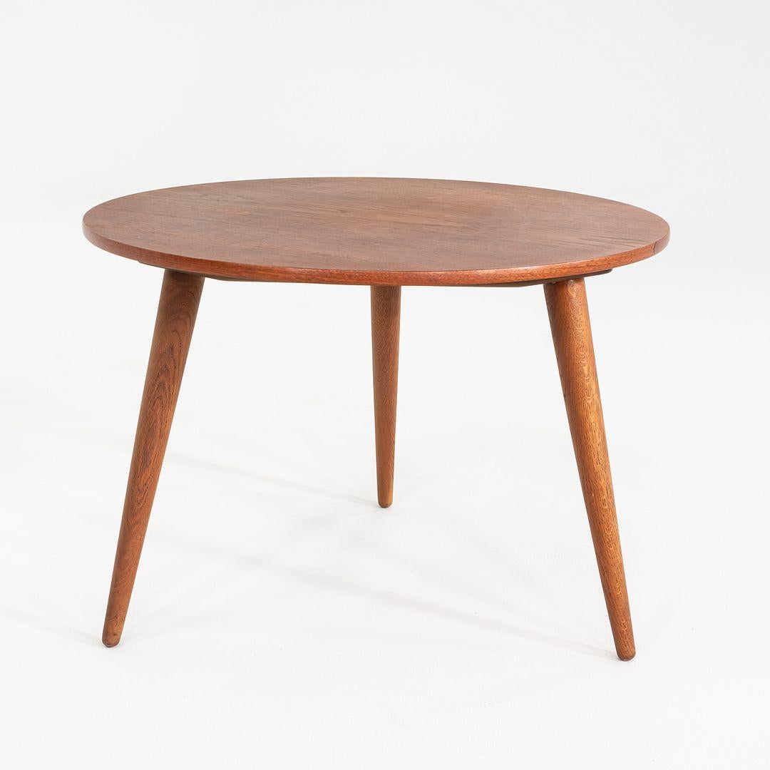 This is a Round Side/End or Coffee Table, Model AT008 (now called the CH008), designed by Hans Wegner and produced by Andreas Tuck in Denmark. It features a circular teak top and has tapered stained oak legs. With only three legs, the table is also
