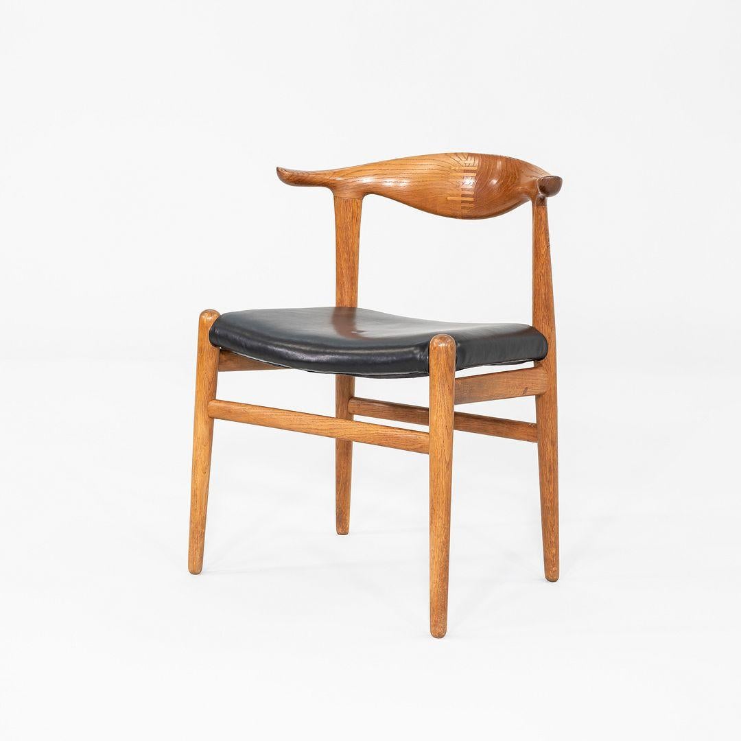 This is a JH505 Cow Horn Chair, originally designed by Hans Wegner for Johannes Hansen in 1952. This particular example was produced in Denmark in the 1960s. The chair features a solid frame of lacquered oak and has an upholstered black leather