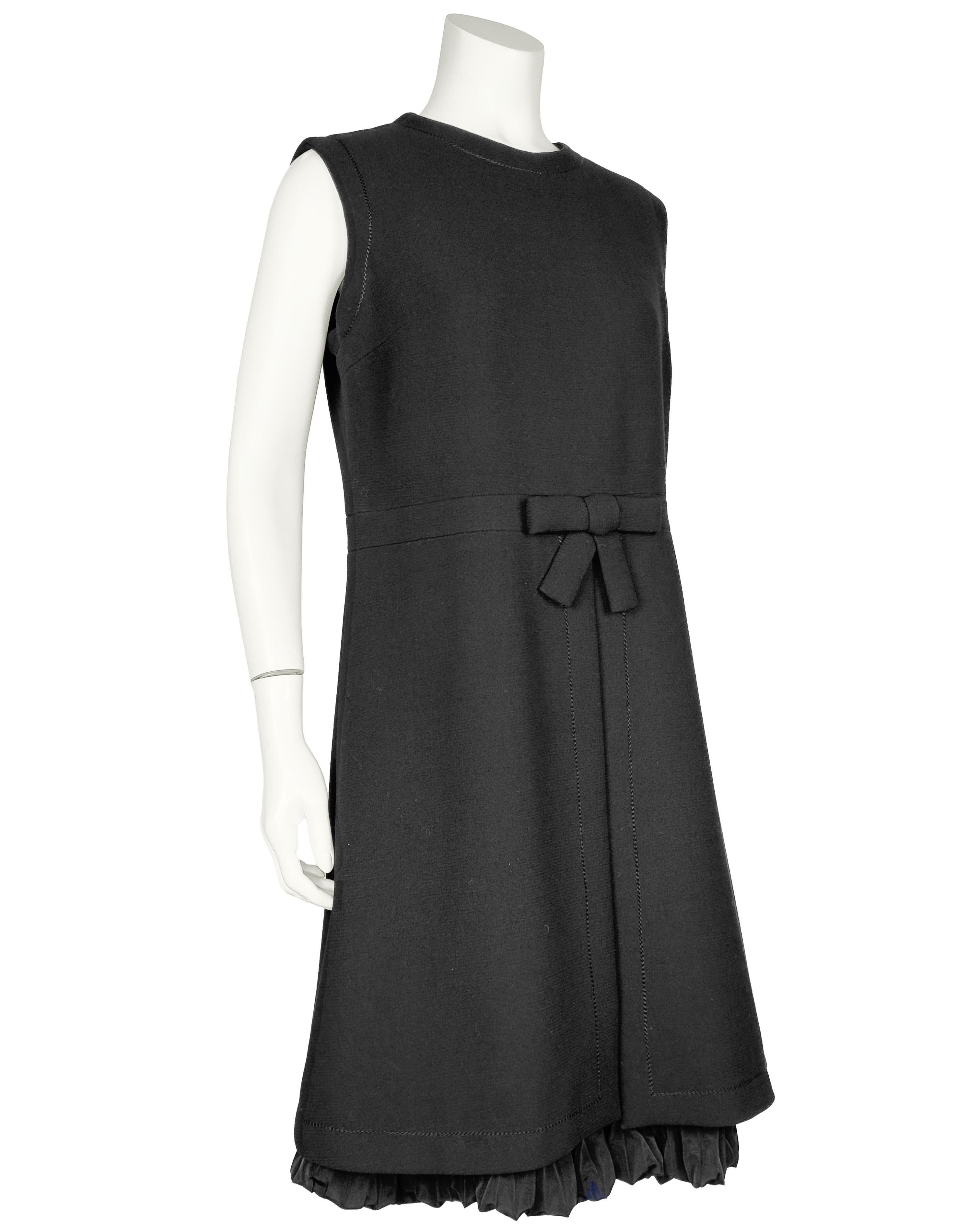 Mod with a twist 1960s Harry Algo black wool crepe little black dress. Sleeveless with a round neck. Fitted through the body with a flat bow to accent the waist. The skirt is a line in shape with a slit up the centre seam that reveals a pleated silk