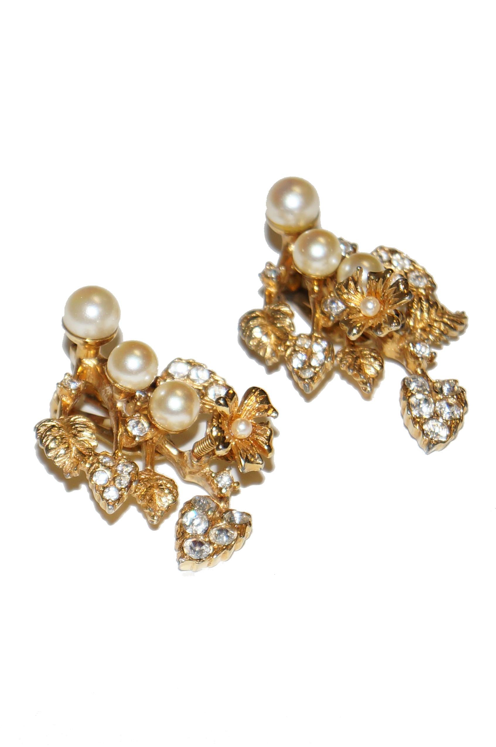 This opulent set of gold tone pearl and rhinestone earrings is indicative of the luxurious jewelry Hattie Carnegie designed in the 1950s and 1960s. The earrings features a wide spray floral design composed of various rhinestone encrusted leaves with