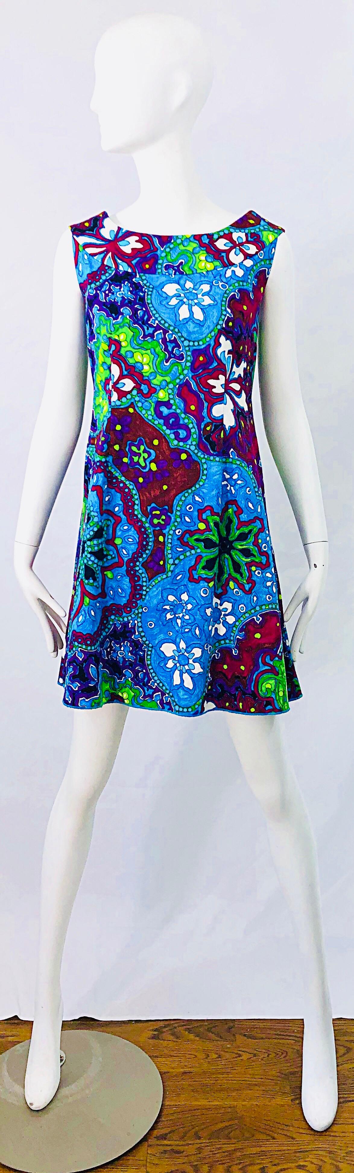 Chic vintage 60s Hawaiian flower print vibrant colored A-Line trapeze mini dress ! Features bright colors of blue, turquoise, purple, burgundy, red and white throghout. Higher front neck that dips in the back. Hidden zipper up the back with