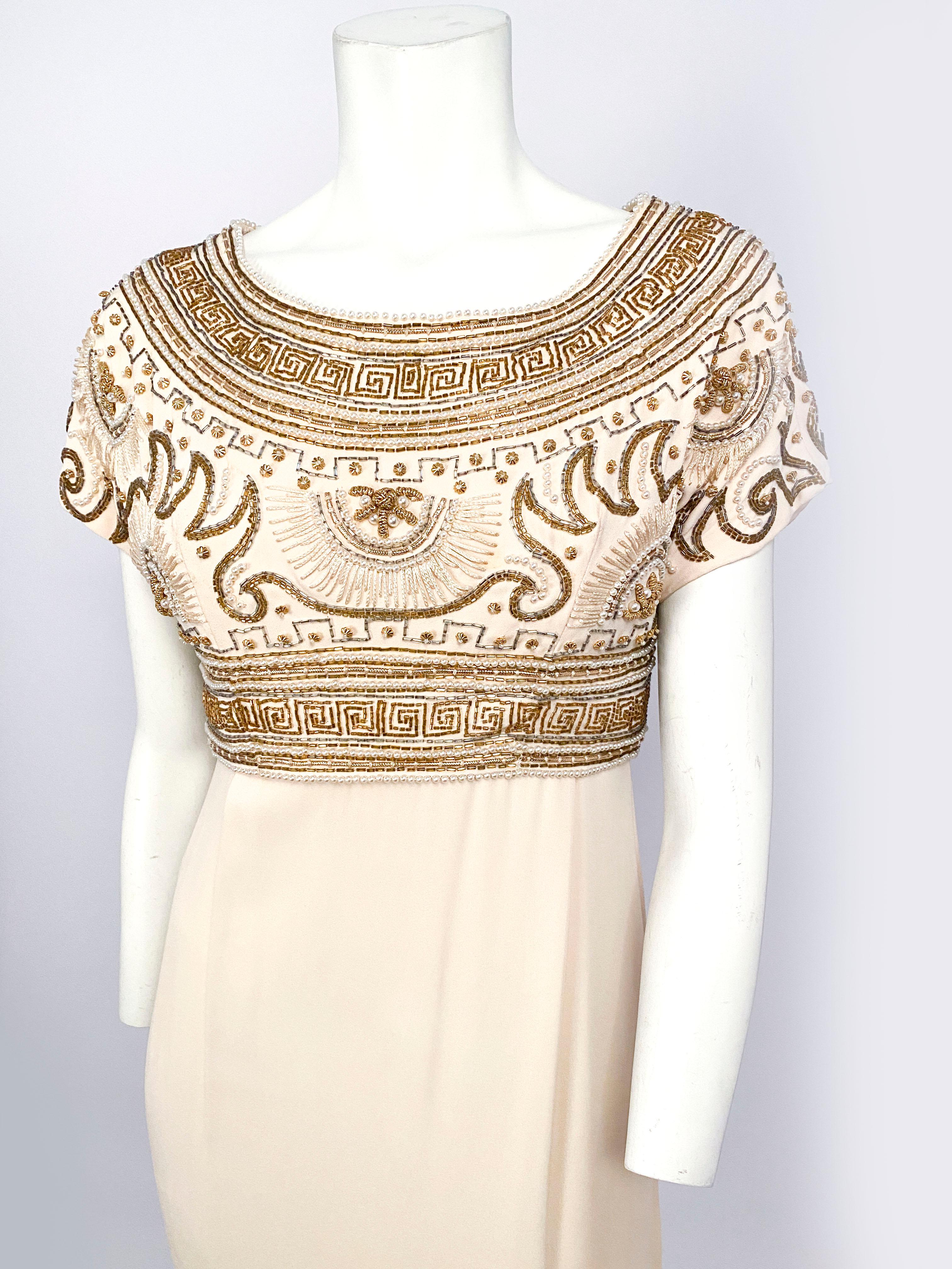 1960s Helen Rose full-length evening gown in a cream silk chiffon featuring ornate beadwork and embroidery with pearls, glass beads, and brass decoration. Beading is along the bottom of the skirt and the removable top and features Egyptian patterns