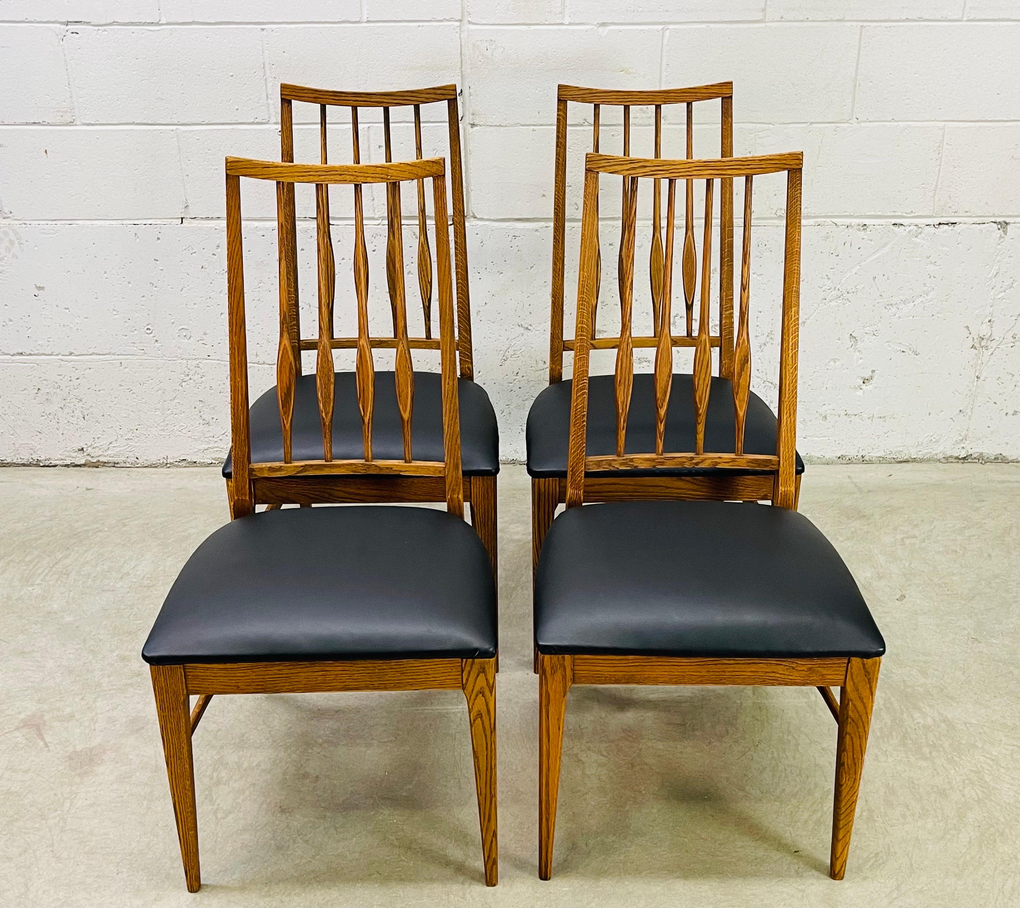 Vintage 1960s set of four oak and ash wood high-back dining room chairs with black naugahyde seats. The dining chairs have a curved back and are very comfortable to sit in. The chairs are in newly refinished condition and are all sturdy. No marks.