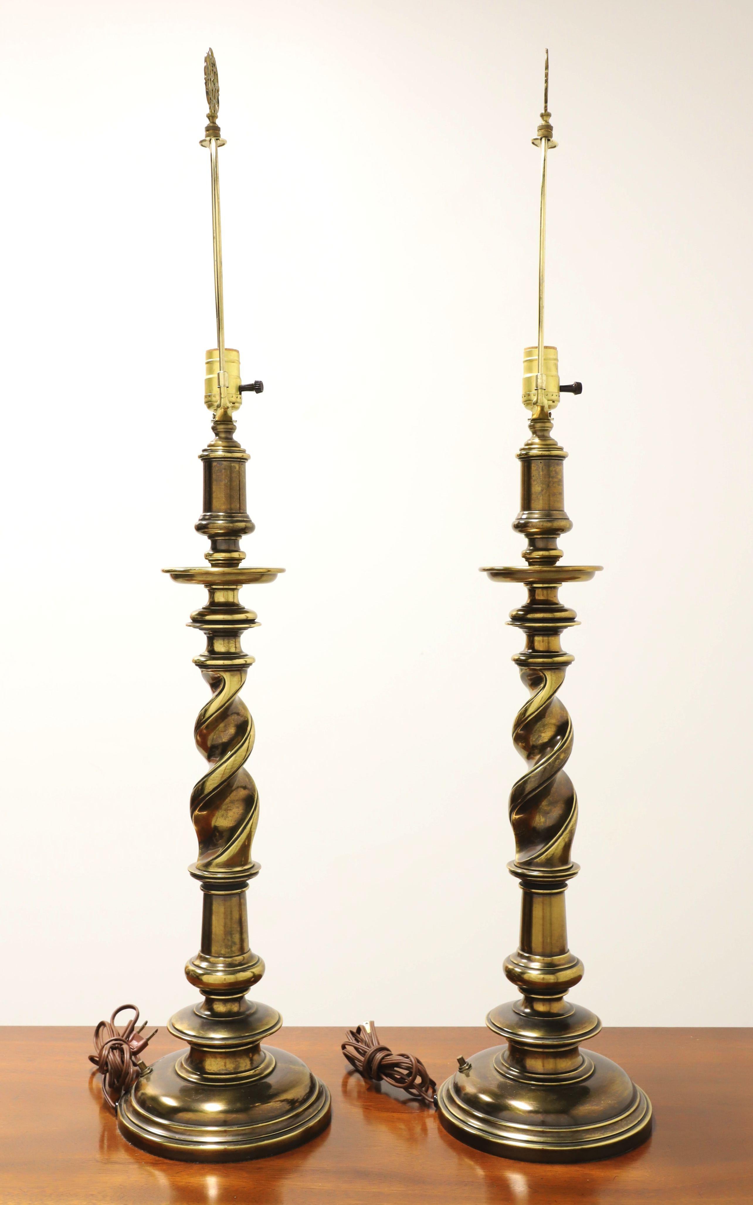 A pair of Hollywood Regency style table lamps, unbranded. Made of solid brass with a candlestick shape, distinctive barley twist design, and a brass base. Has a removable metal harp and decorative brass filigree finial. Single standard bulb socket
