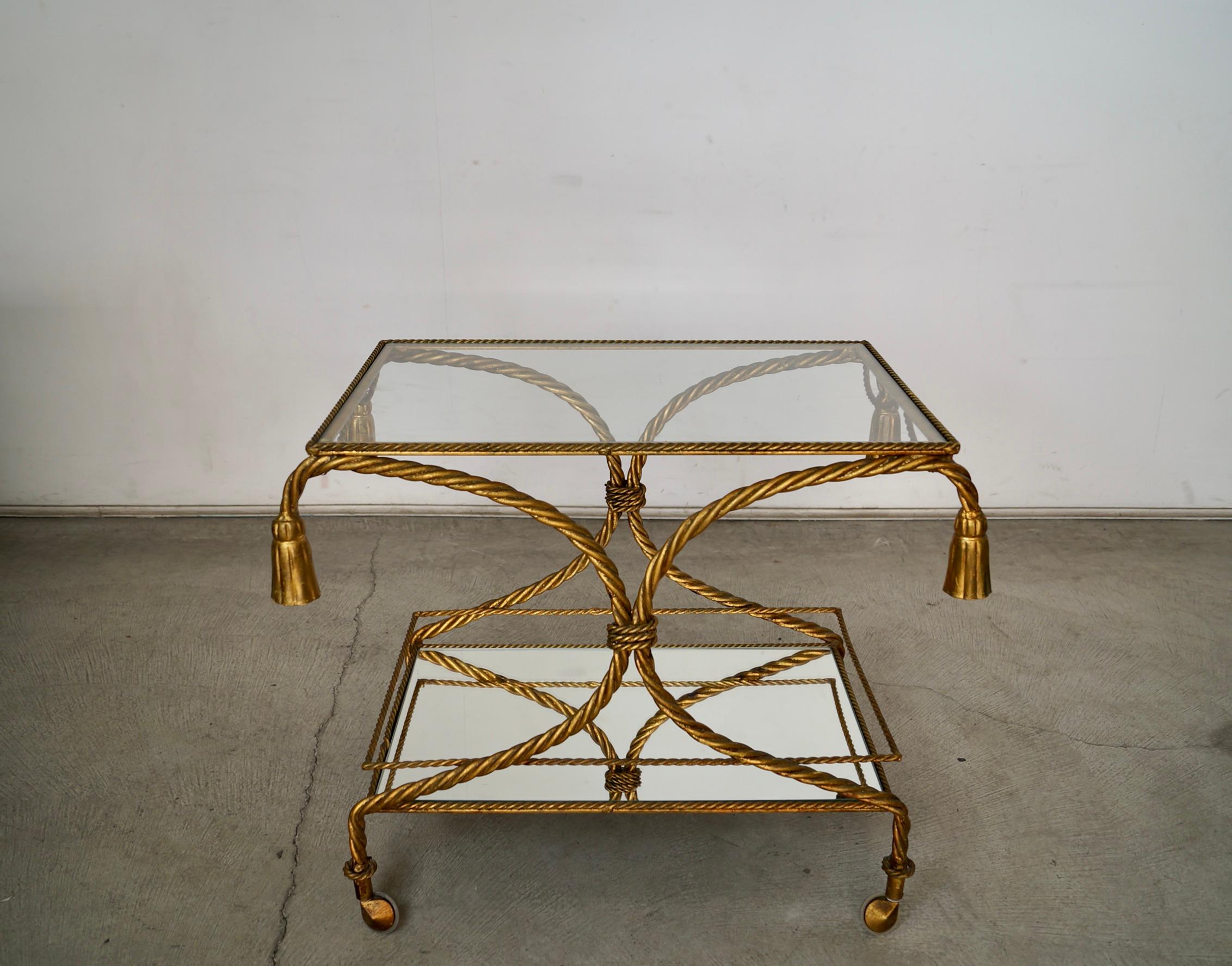 Vintage Hollywood Regency bar cart trolley for sale. It's made of metal, and displays incredible craftsmanship. It has a tassel rope design on the metal, and has a gilded gold leaf finish. It's really solid and well made, and rolls smoothly. It was