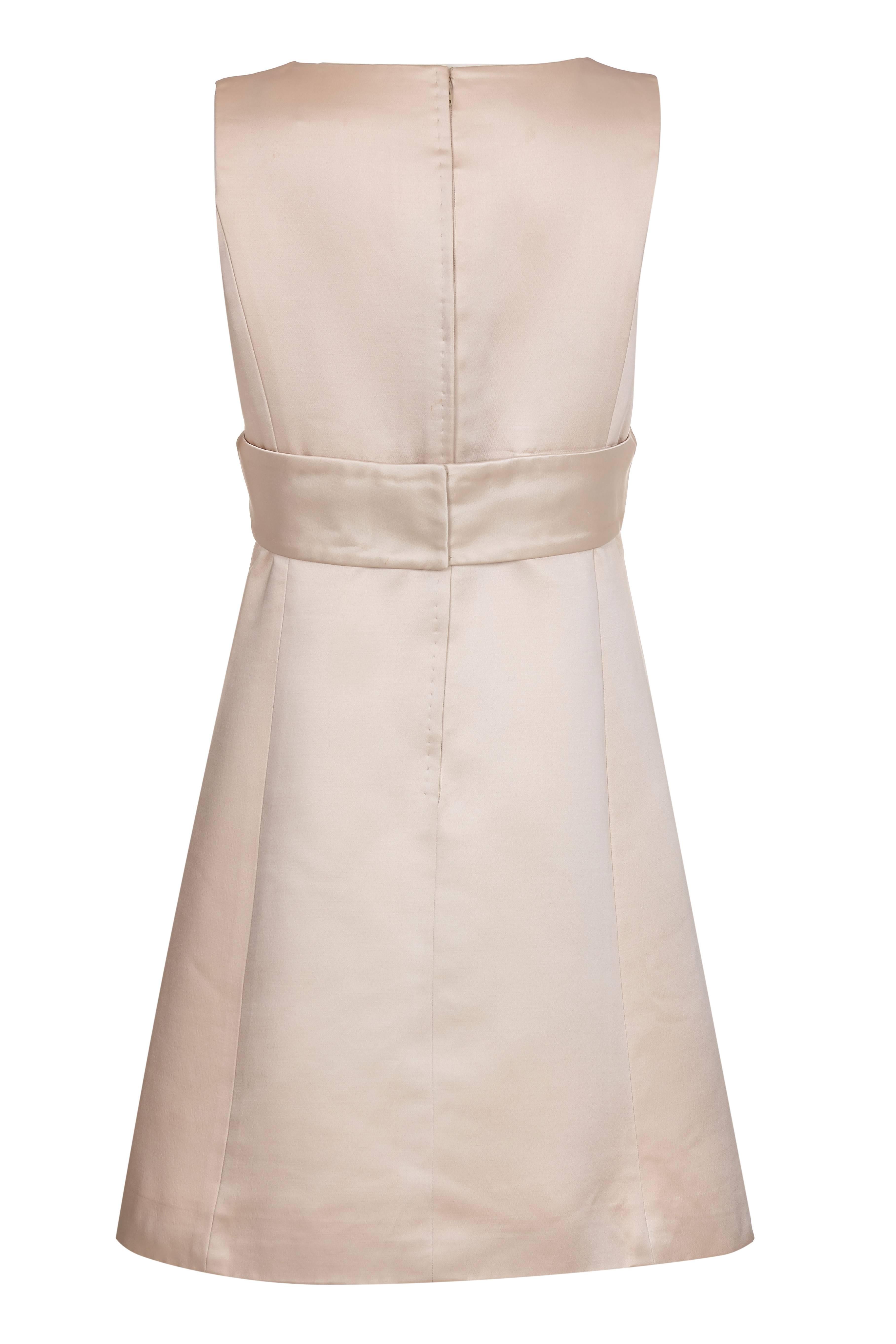 Este clásico y chic vestido vintage de satén de seda color crema de los años 60, de los prestigiosos grandes almacenes I. Magnin and Co de San Francisco, es de una calidad excepcional. El vestido no lleva mangas y tiene el busto cruzado con un