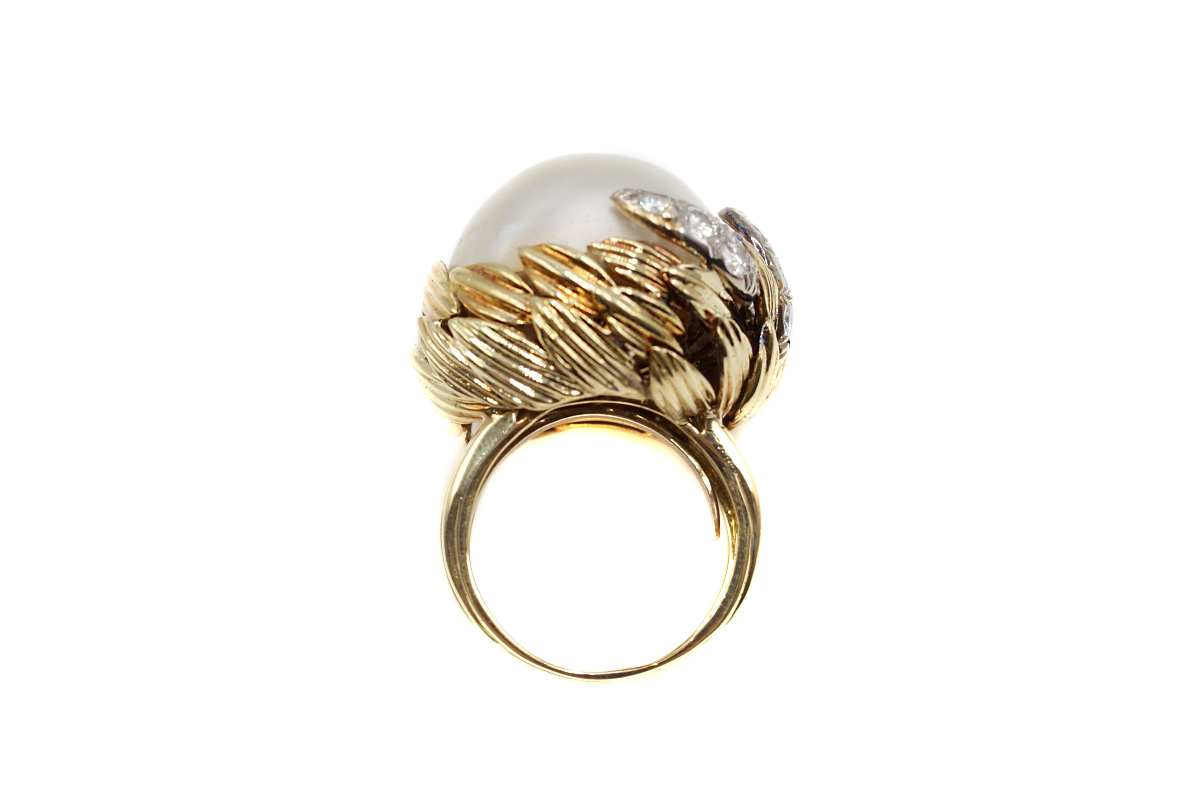 This bold 60s ring features an impressive Mabe Pearl with over 23 millimeters in diameter. The beautifully hand-crafted 18 karat yellow gold mounting has a double row of finely textured leaves surrounding and holding the pearl with 3 of the petals