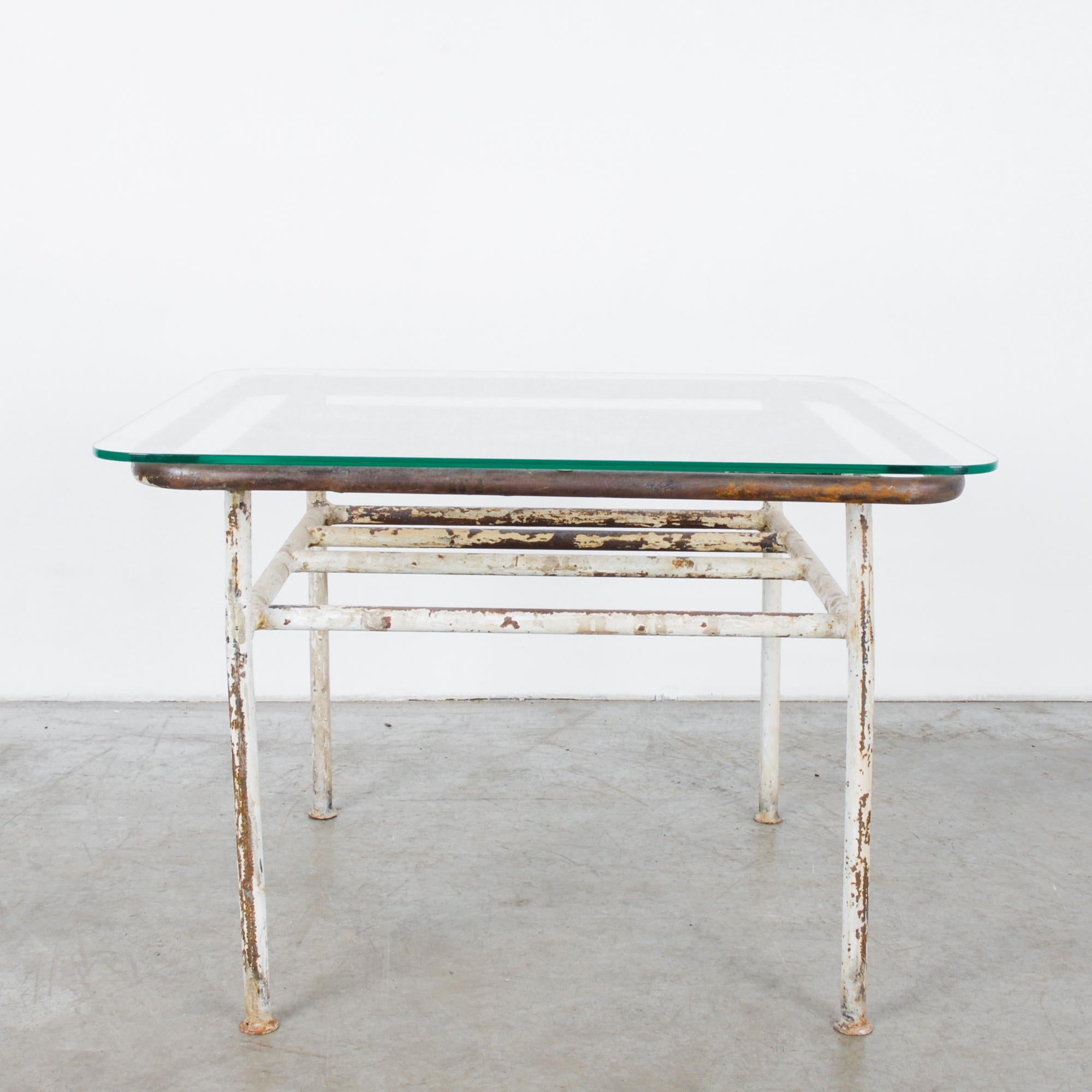 This coffee table was made in France, circa 1960. The clear glass tabletop features rounded edges and rests on a frame constructed from metal tubes. Originally painted white, the metal frame displays a timeworn patina, offering a lived-in,