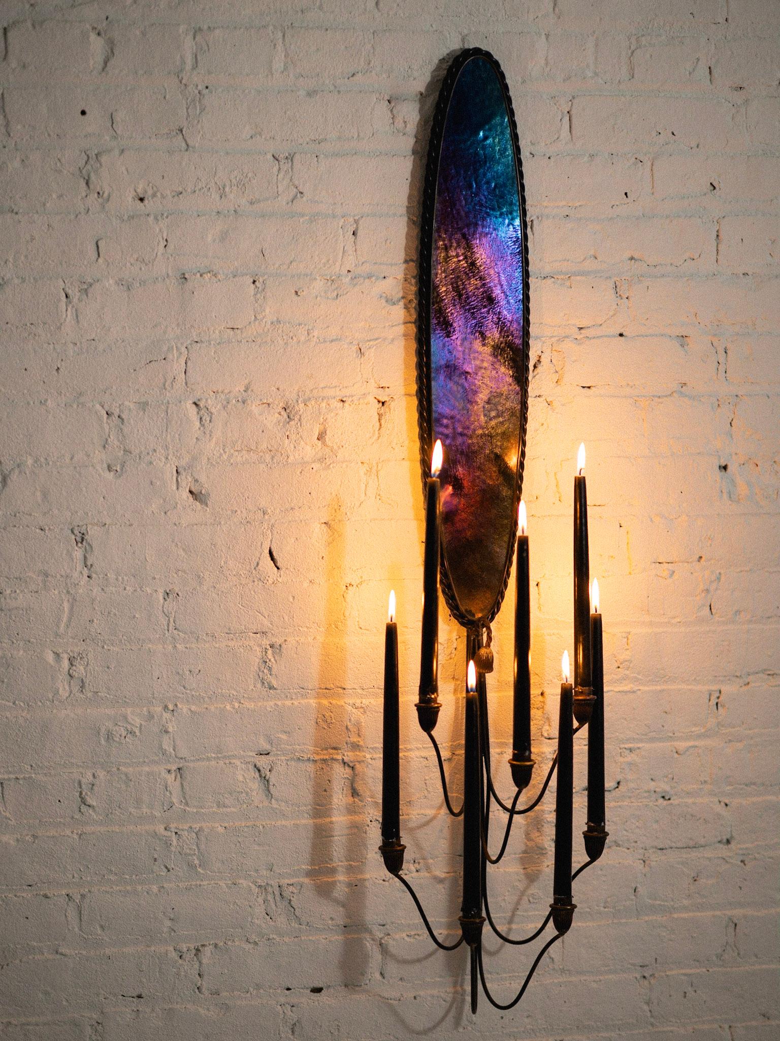 A 1960s candle sconce. Consists of a panel of iridescent glass framed by twisted iron. Seven fluted brass heads elevate to hold taper candles. Lovely patina throughout. Pair available. Sold separately.
