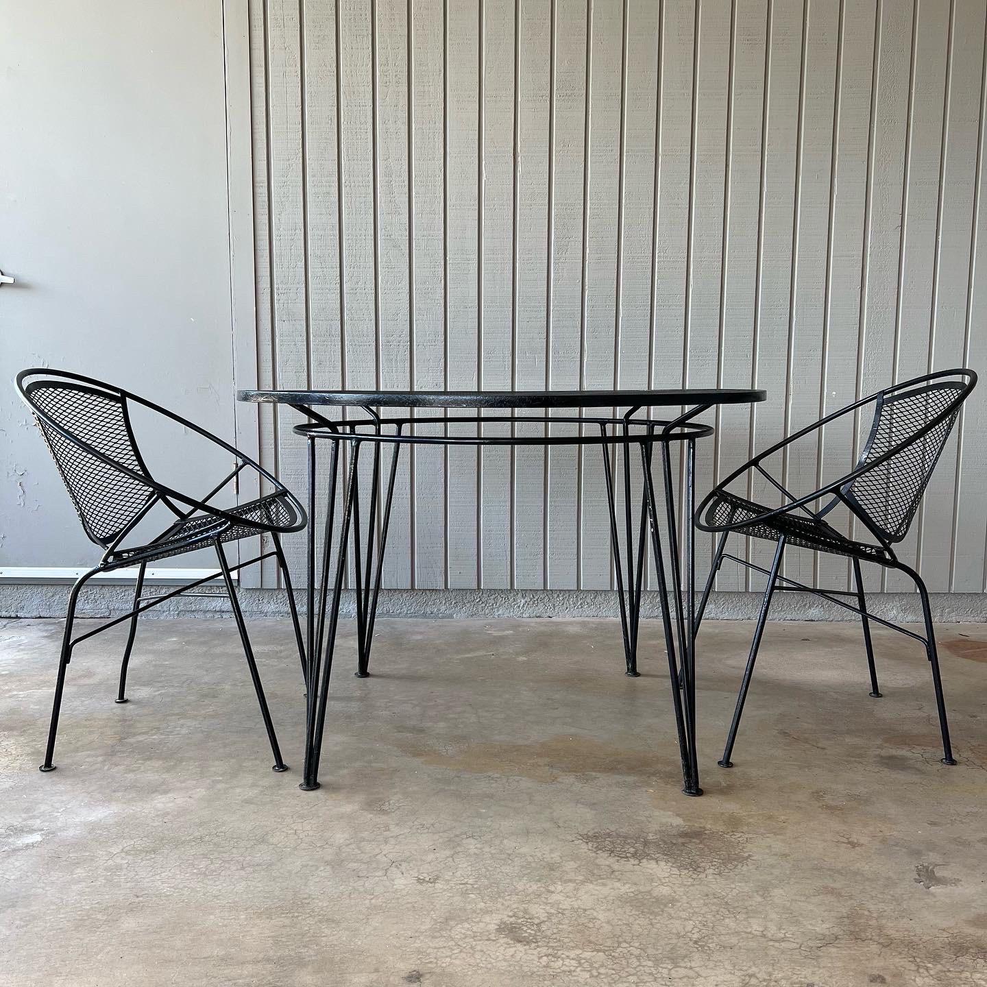 Wrought iron patio Salterini “Radar” Collection bistro set with two hoop dining height chairs and a table. Designed by Maurizio Tempestini, 1960s. One chair leg has a slight bend as pictured but still functions just fine. Each chair measures 21”