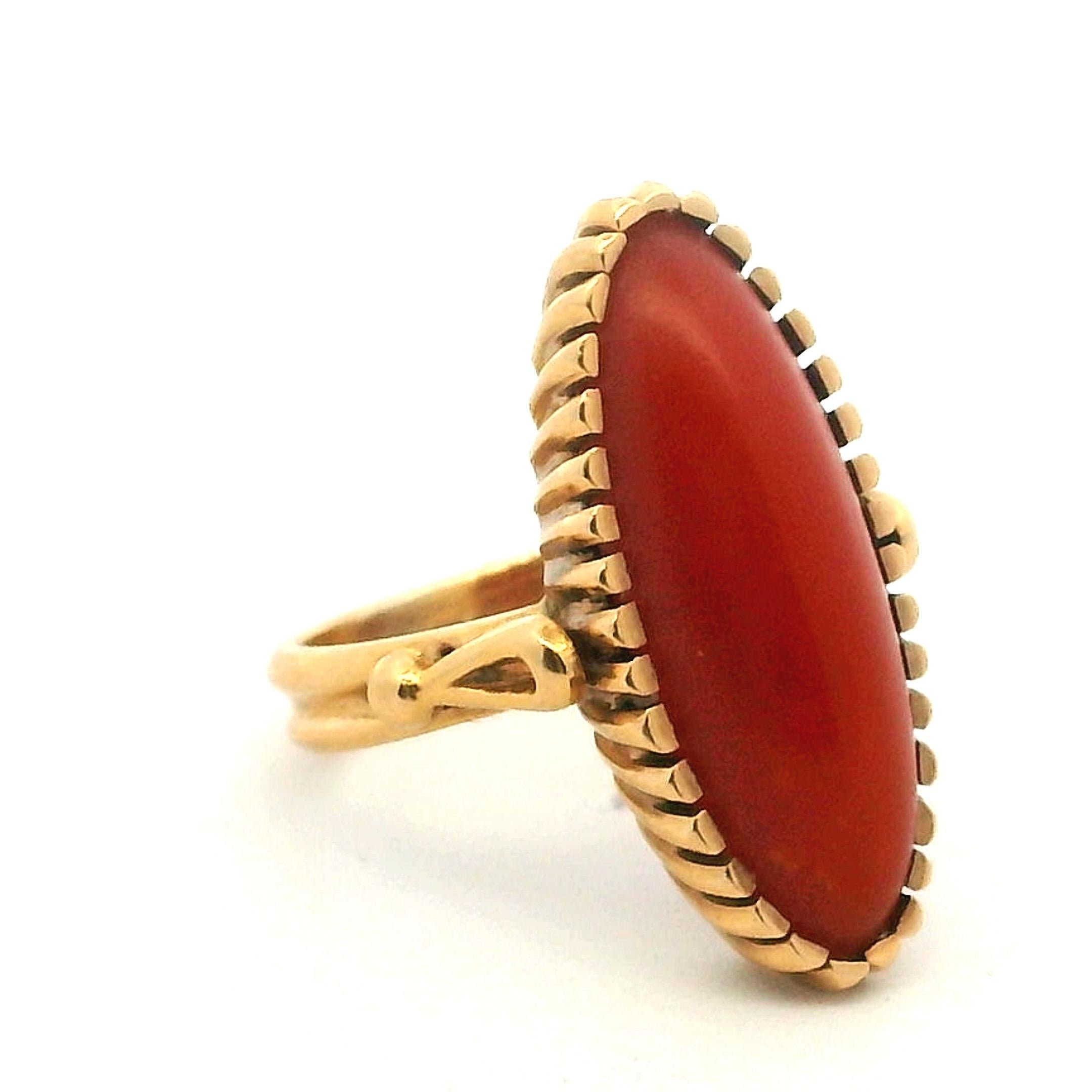 Uno squisito anello italiano degli anni '60, magistralmente realizzato in oro giallo 18 carati e caratterizzato da un magnifico cabochon di corallo rosso naturale a forma di navetta allungata, che misura circa 21,5 x 8,2 mm. Il corallo presenta una