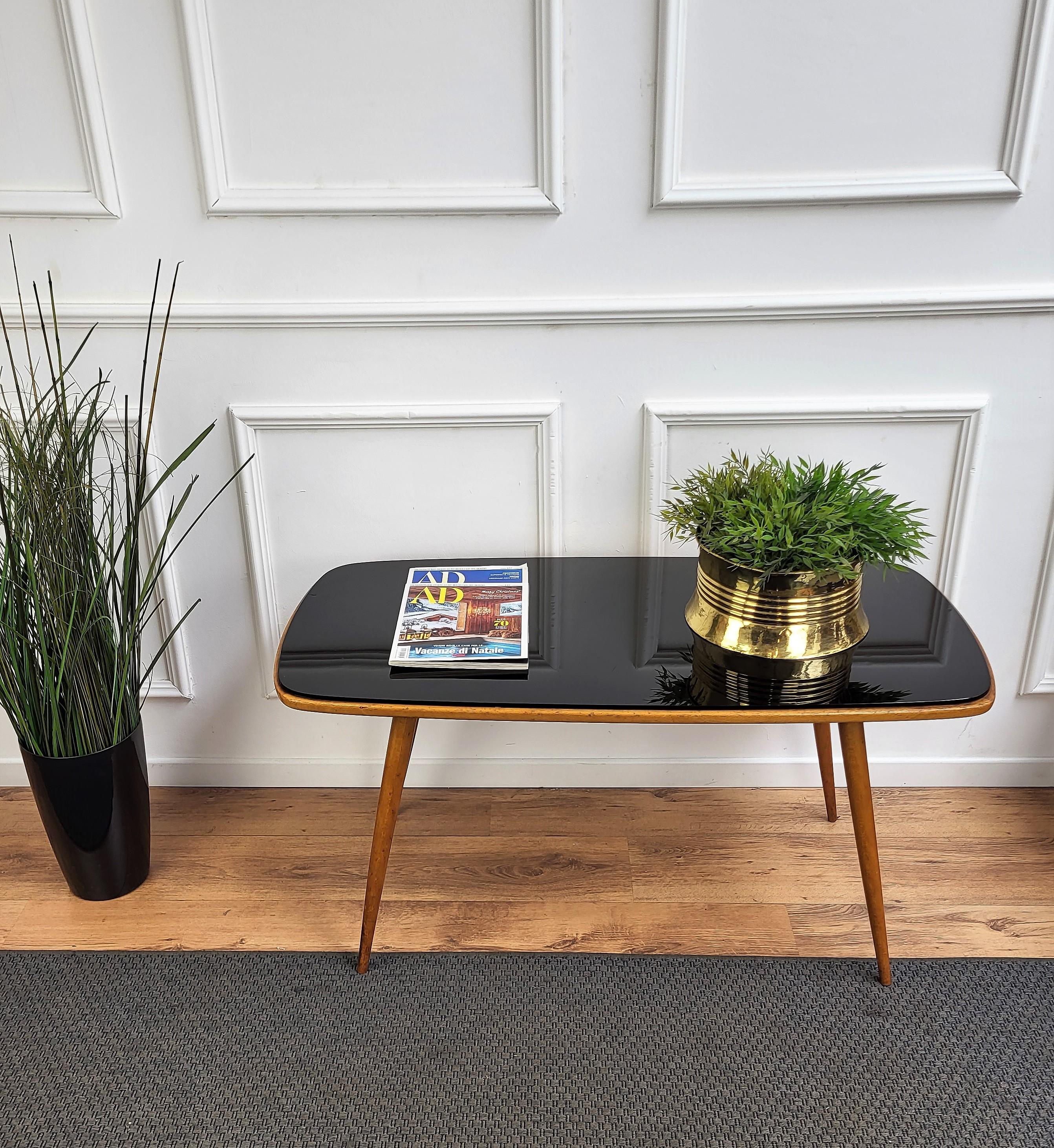 Very elegant and typical Italian Mid-Century Modern coffee or side table, oval shaped and with stylish legs. This beautiful piece is completed by the black glass top.