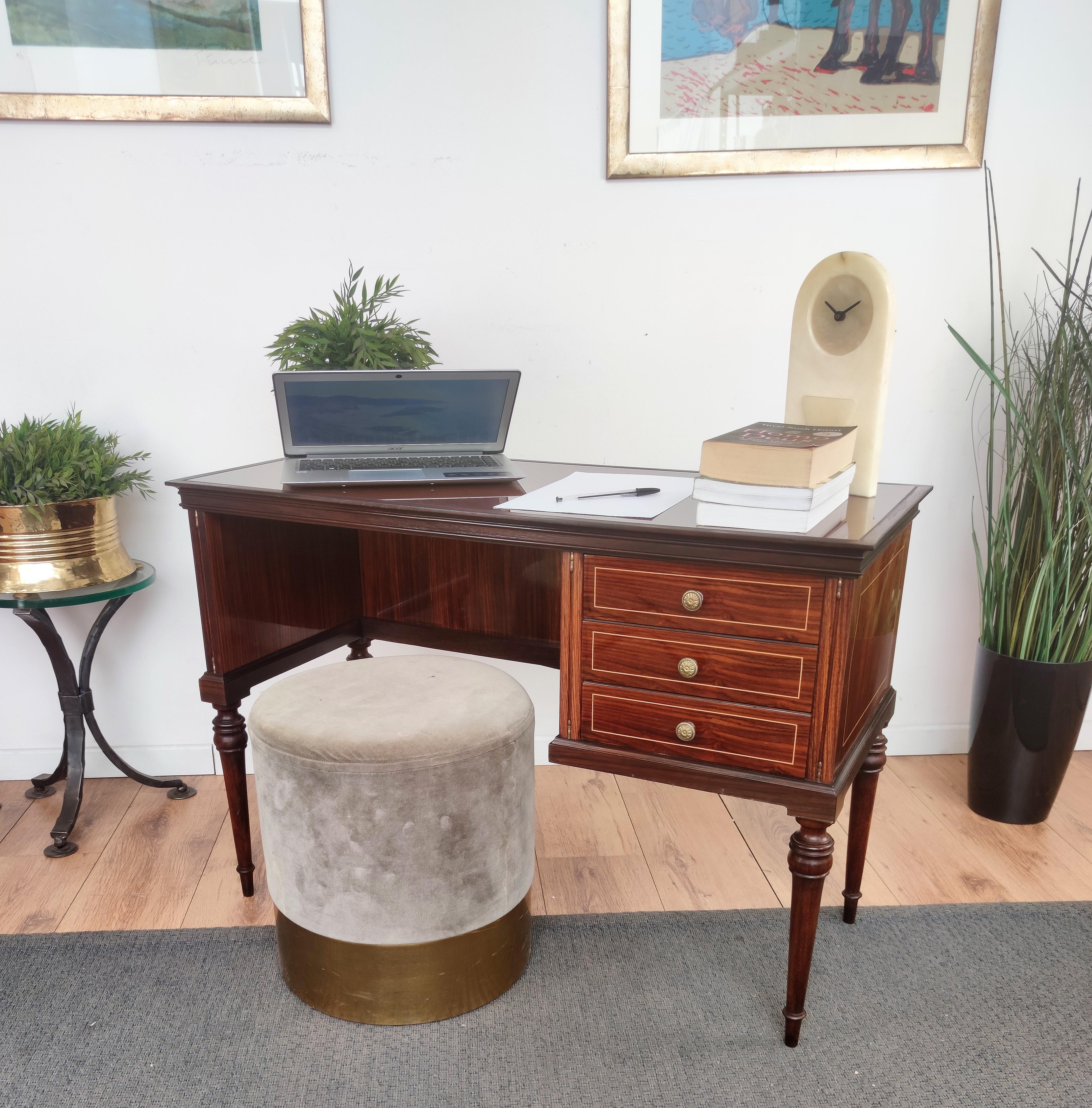 Very elegant Italian Art Deco Mid-Century Modern small desk or writing table secretaire, in beautiful decorated and veneer wood with three drawers and covered sides. This beautiful piece is completed by the bordeaux glass top, the brass drawers