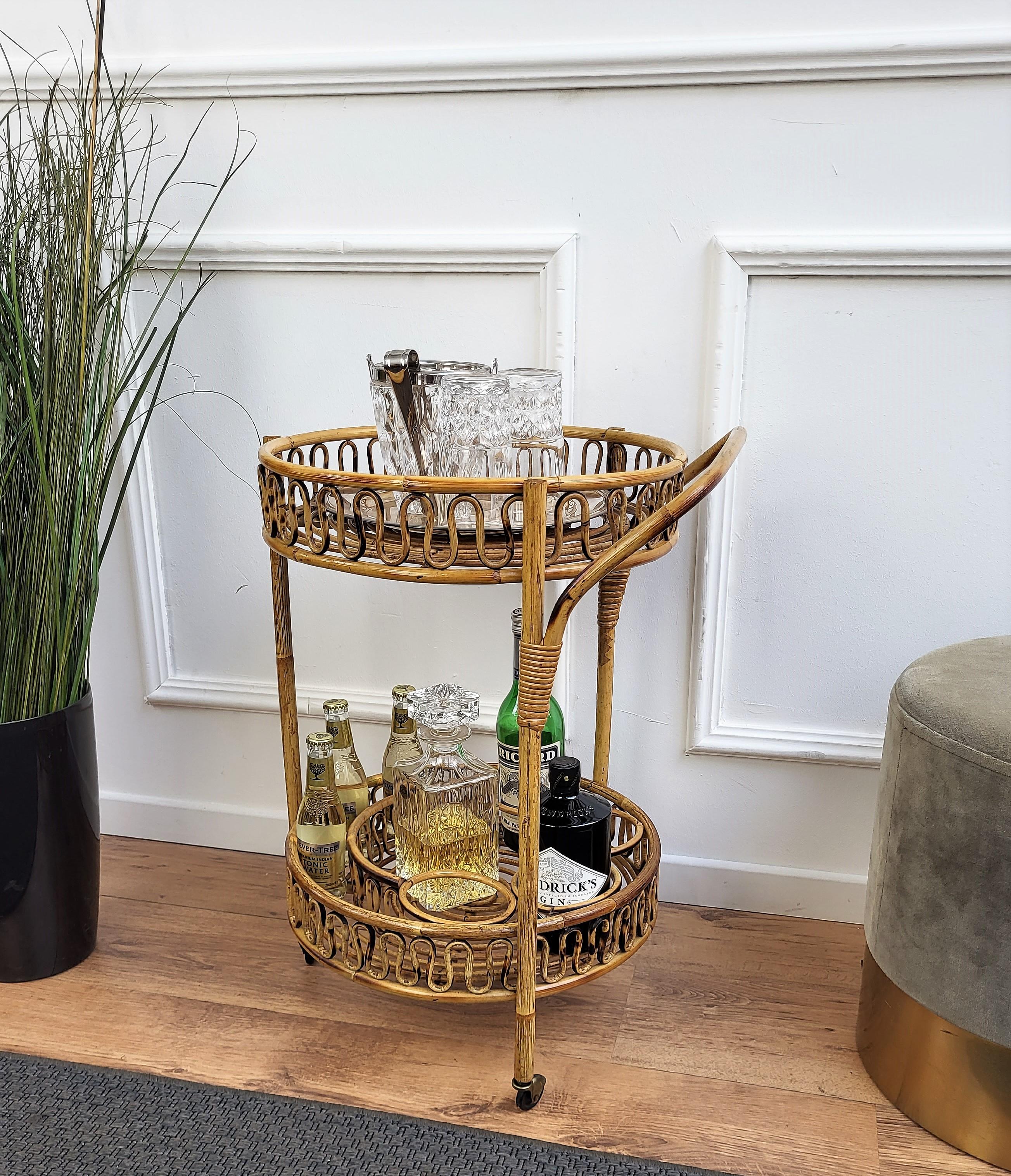 Beautiful 1960s Italian Mid-Century Modern serving bar cart trolley probably by the Italian Vittorio Bonacina featuring two shelves, with the bottom one with three bottle holders. Made of rattan and bamboo. This charming piece is in the typical