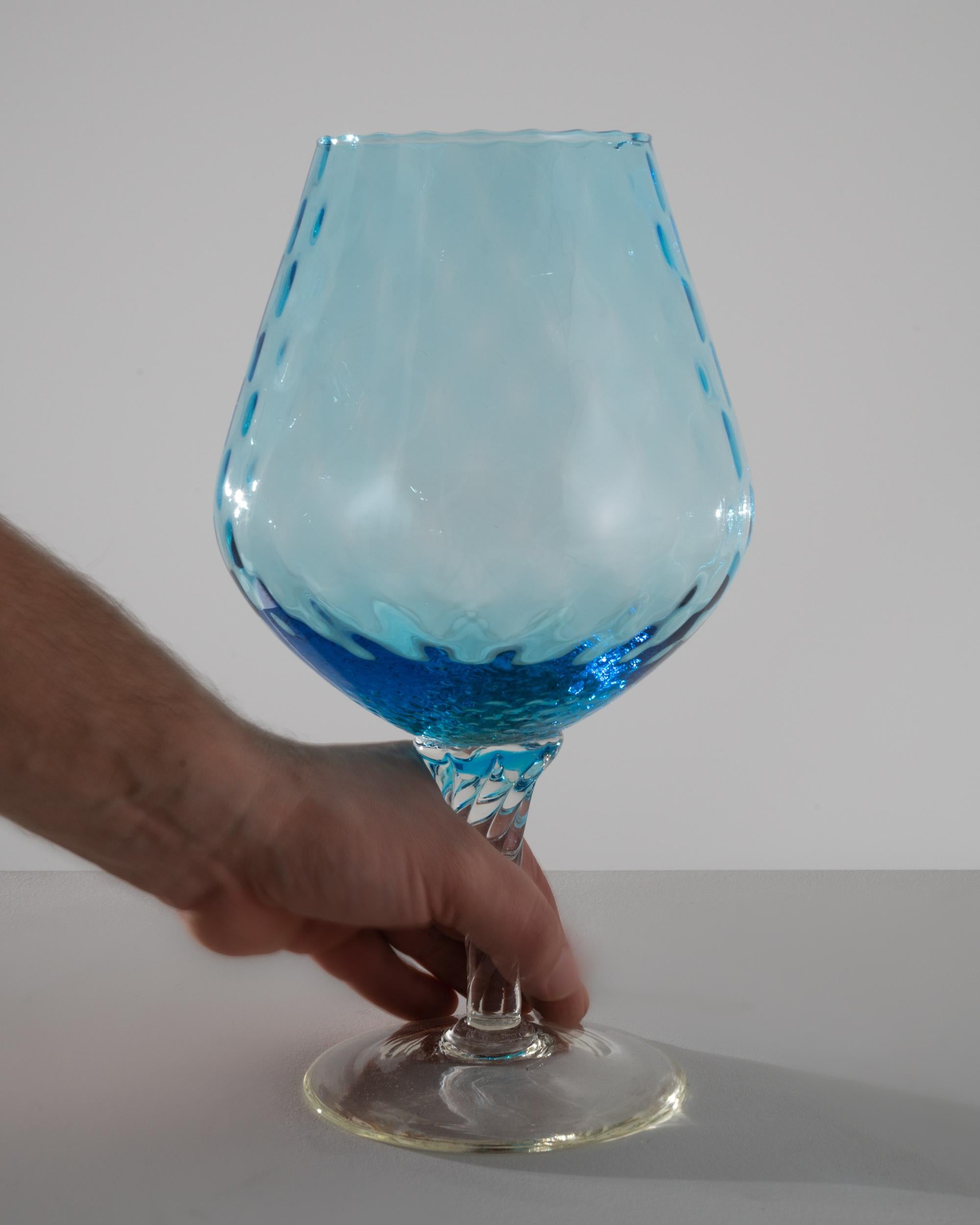 Discover a piece of history with this exquisite 1960s Italian Blue Glass Goblet, a testament to timeless craftsmanship. The goblet boasts a unique, rounded bowl, adorned with a subtle wave pattern that resembles the gentle ripples of the