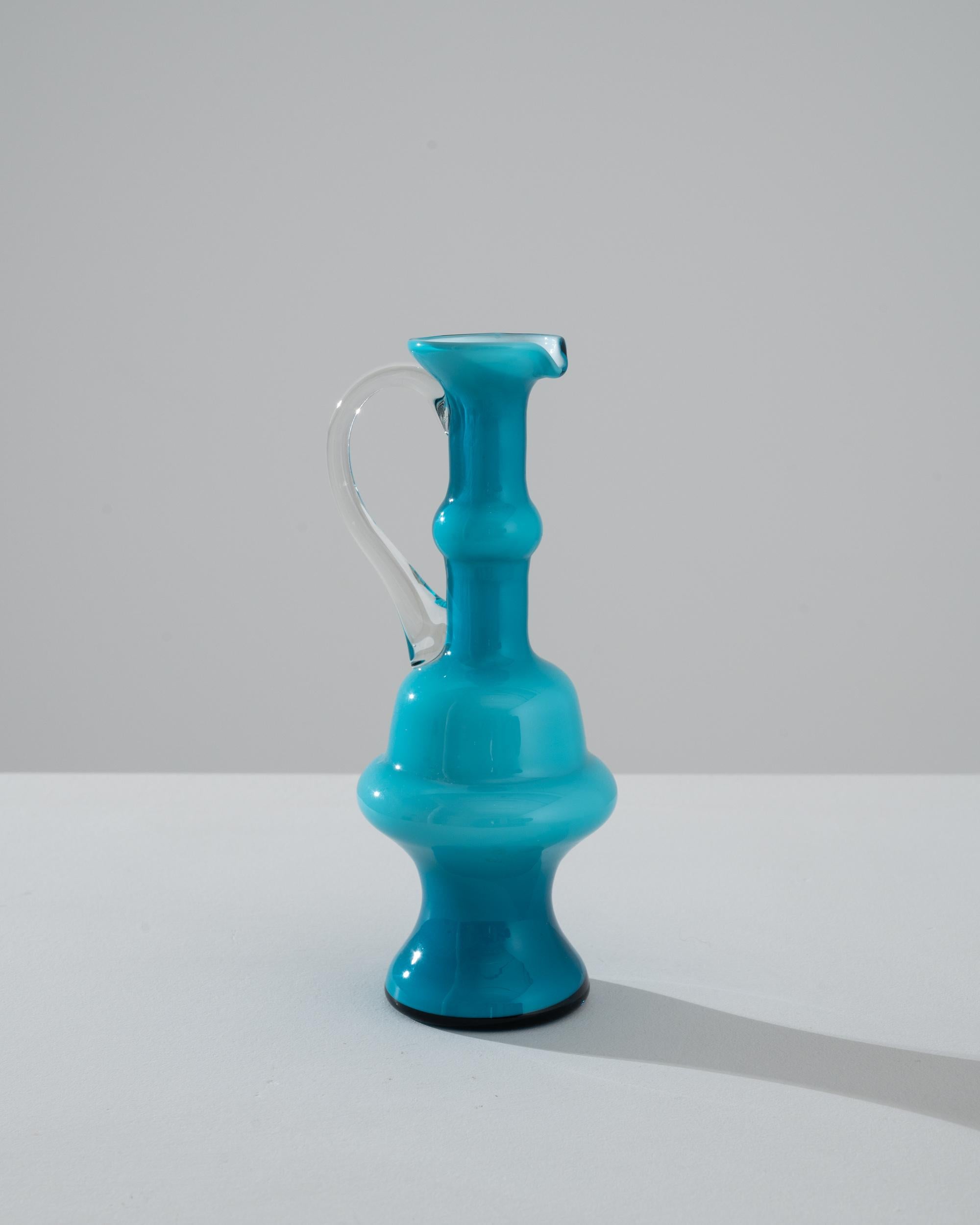 Admirez un morceau de l'histoire italienne avec cette superbe cruche en verre bleu italien des années 1960, une incarnation de la forme et de la fonction en une seule création artistique. Le verre bleu aqua vibrant, méticuleusement façonné en un