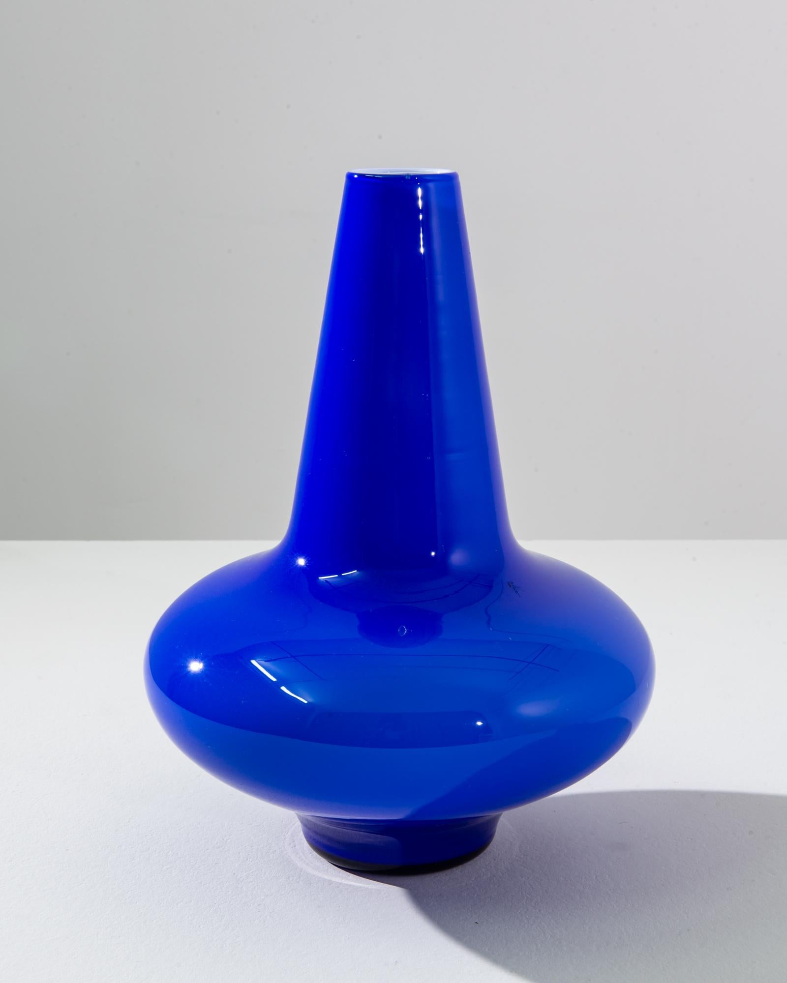 This striking 1960s Italian blue glass vase is a true emblem of mid-century modern design, boasting a vibrant cobalt blue that instantly captivates and adds a splash of color to any room. Its sleek, conical neck gracefully rises from the bulbous
