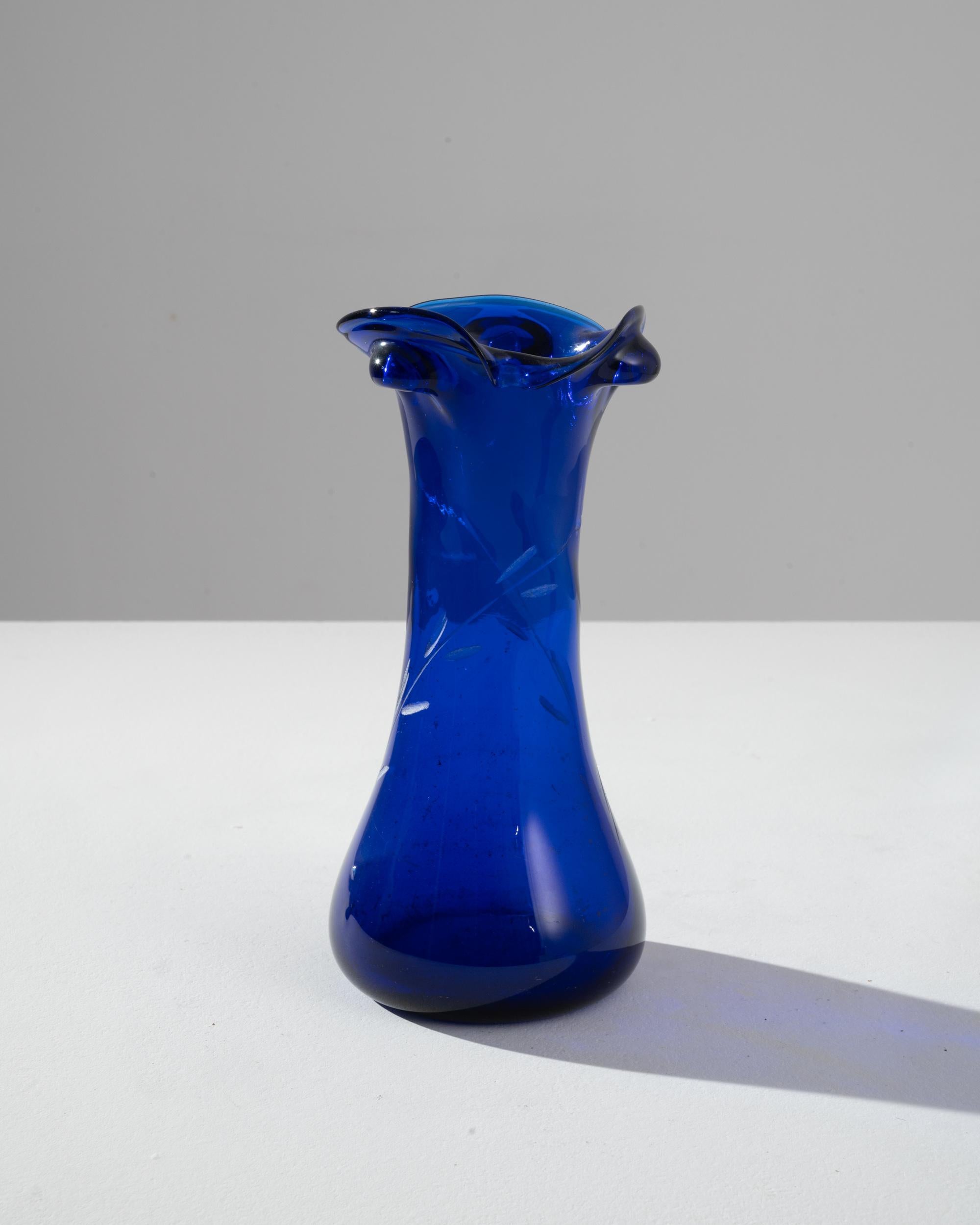 The captivating allure of this 1960s Italian blue glass vase lies in its vibrant cobalt hue and whimsical form. Crafted with a flair for drama, the vase's fluted top ripples elegantly, resembling the petals of an exotic flower. Speckled with subtle
