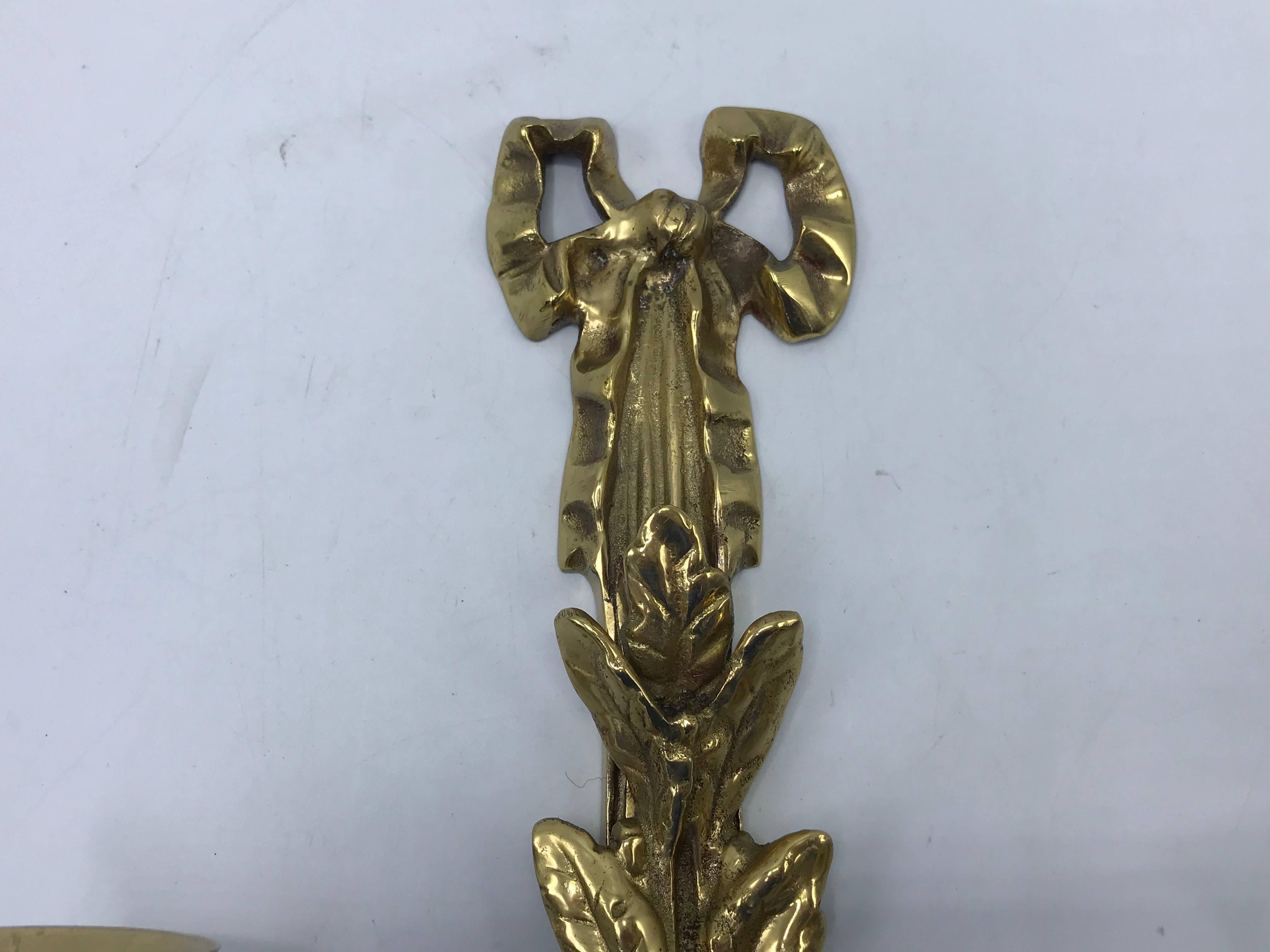 Listed is a fabulous, pair of 1960's solid-brass Italian candlestick wall sconces. The pair has a stunning laurel wreath motif with bow detailing along the top and tassel fringe detailing along the bottom. Heavy. 

We have another pair available,