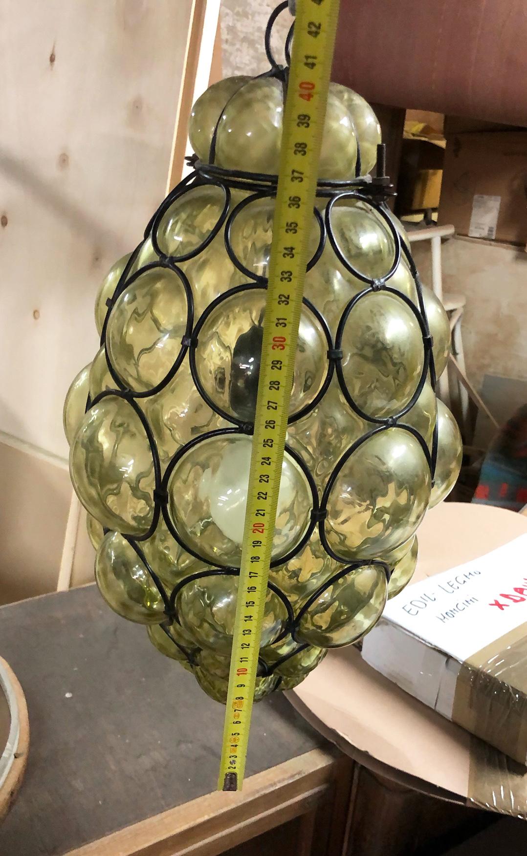 Italian chandelier composed of a light inserted in green bubbles glass in turn inserted in a metal mesh of black color which contains the bubbles.
It has no trademarks but it was certainly produced by a glass factory in Empoli.
The lights have an