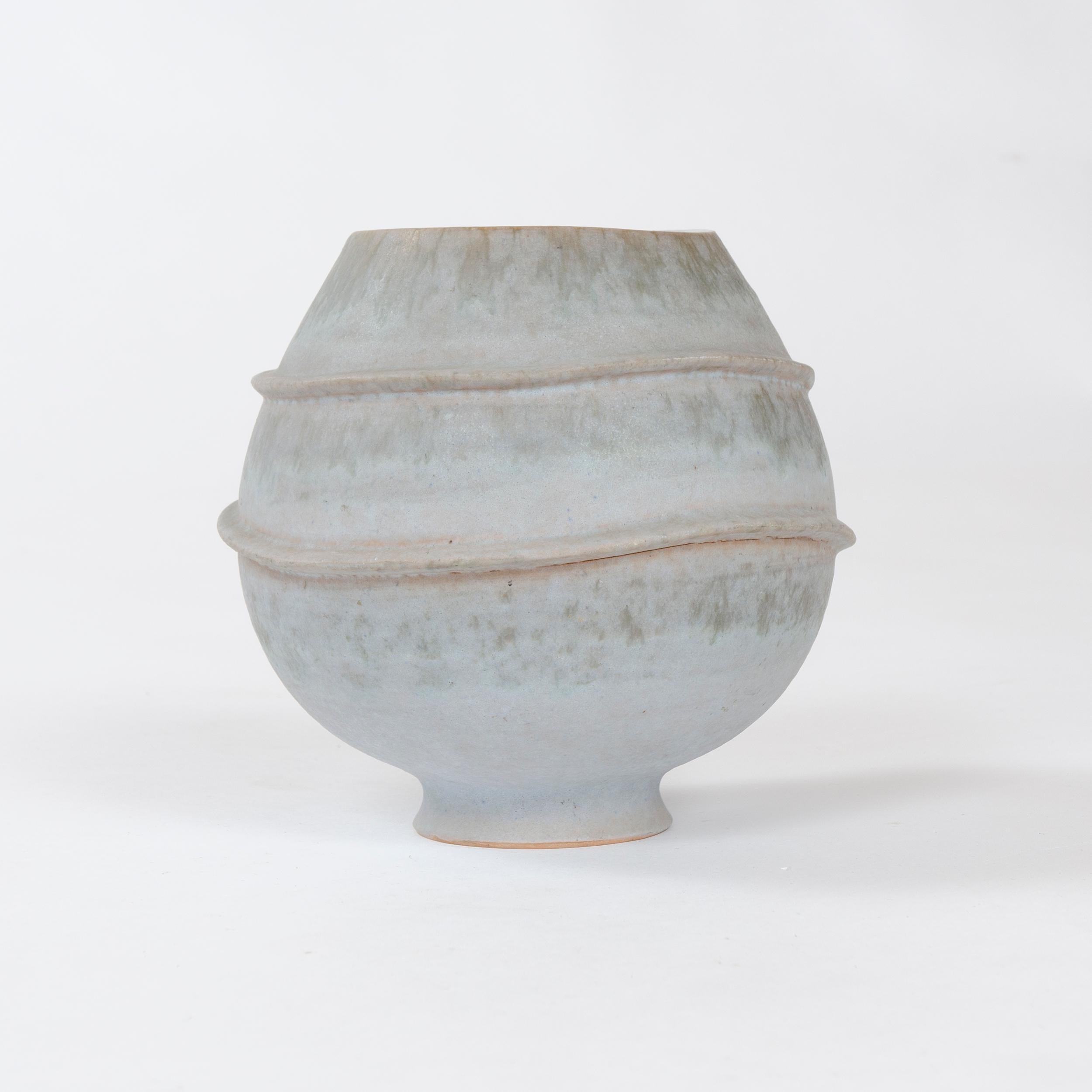 A footed vessel with muted celadon matte glaze accentuated by two undulating circular appliques, with contrasting high gloss glazed interior. Signed 