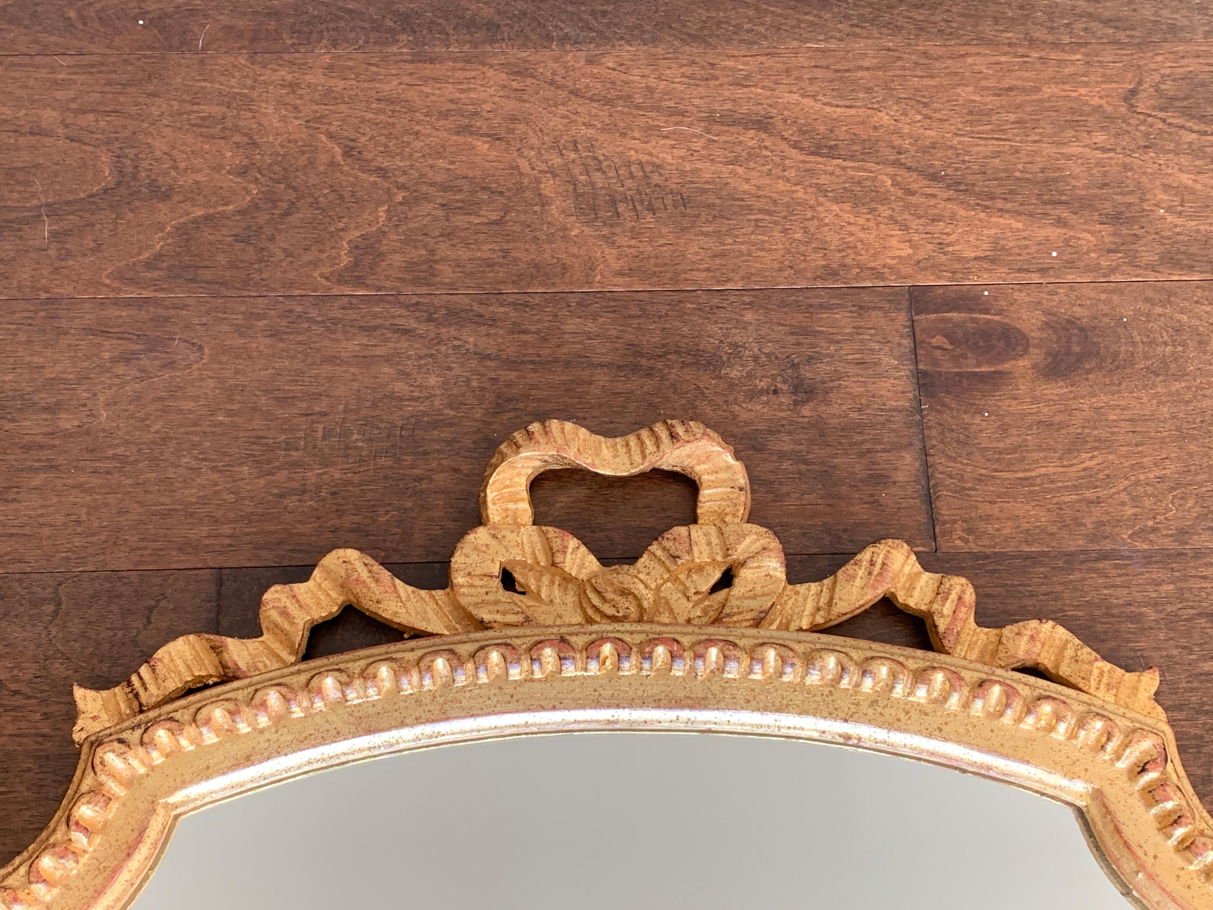 Listed is a gorgeous, Italian giltwood mirror, circa 1950s. The piece has a thick, scalloped wood frame with ribbon detailing. Slight hints of red undertones peak out from beneath the gilding. Heavy, weighing 16lbs. Newly rewired for hanging on