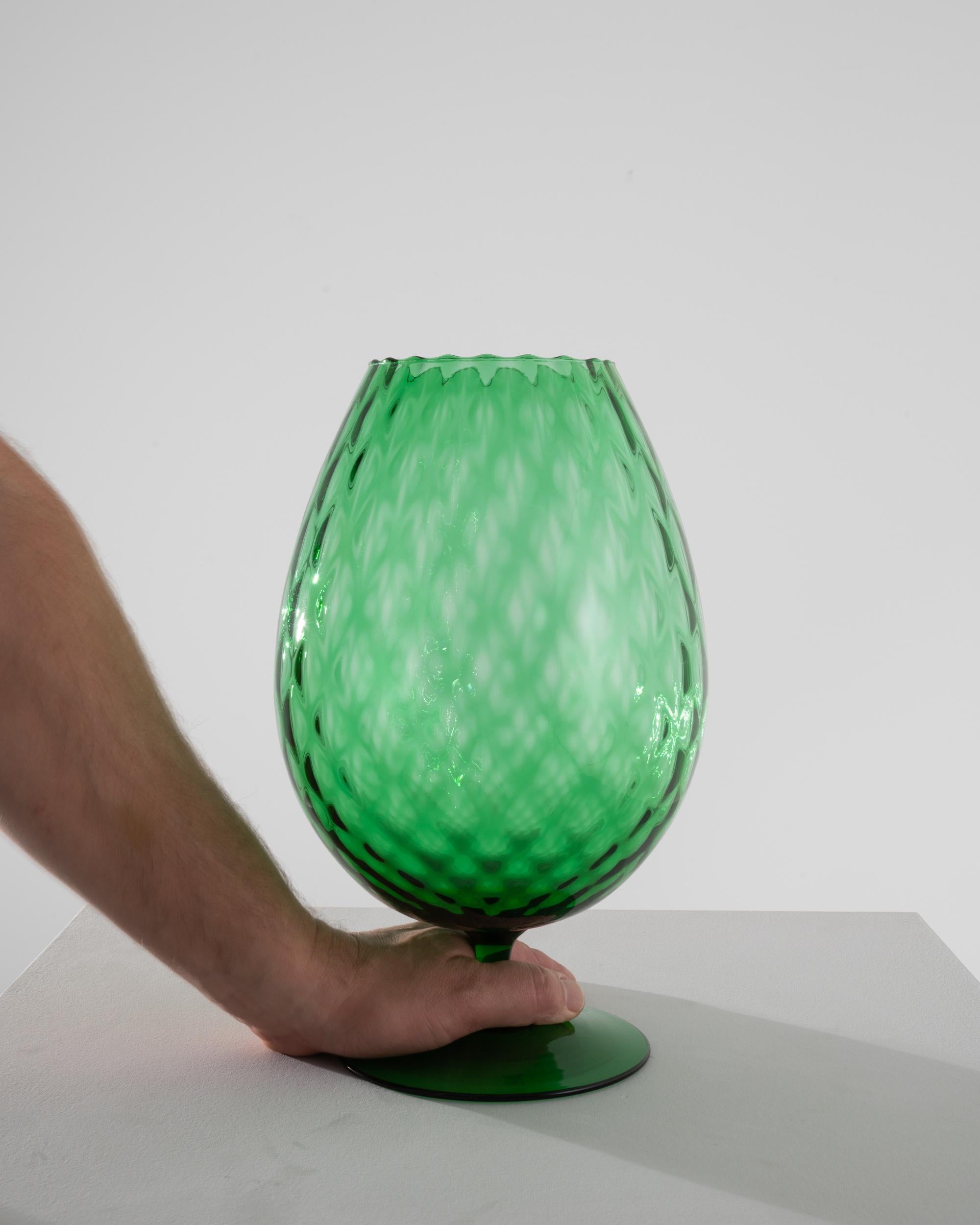 This 1960s Italian Green Glass Goblet is a dazzling piece of vintage charm, evoking the spirit of a bygone era with its vivid, emerald hue and classic design. The body of the goblet features an elegant, diamond-cut pattern, adding texture and
