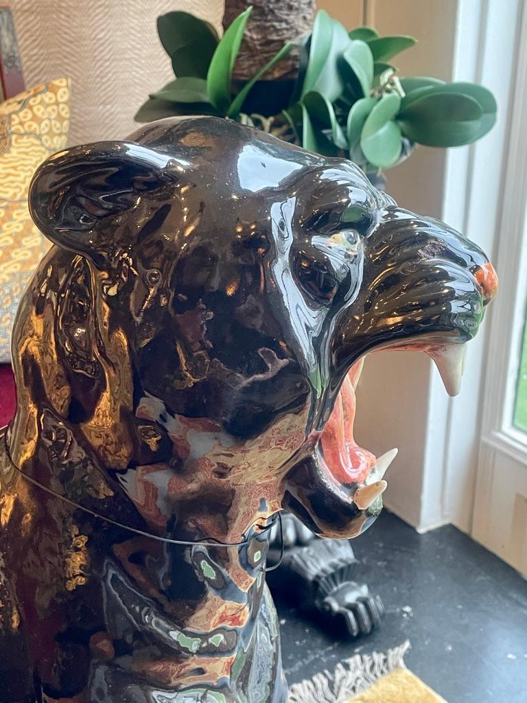 A life-sized ceramic black panther, hand painted with a black body and glass eyes. This Italian 1960s jungle cat is portrayed seated, his tail curling around his front paw, and his snarling jaw wide, showing off his large white canines.