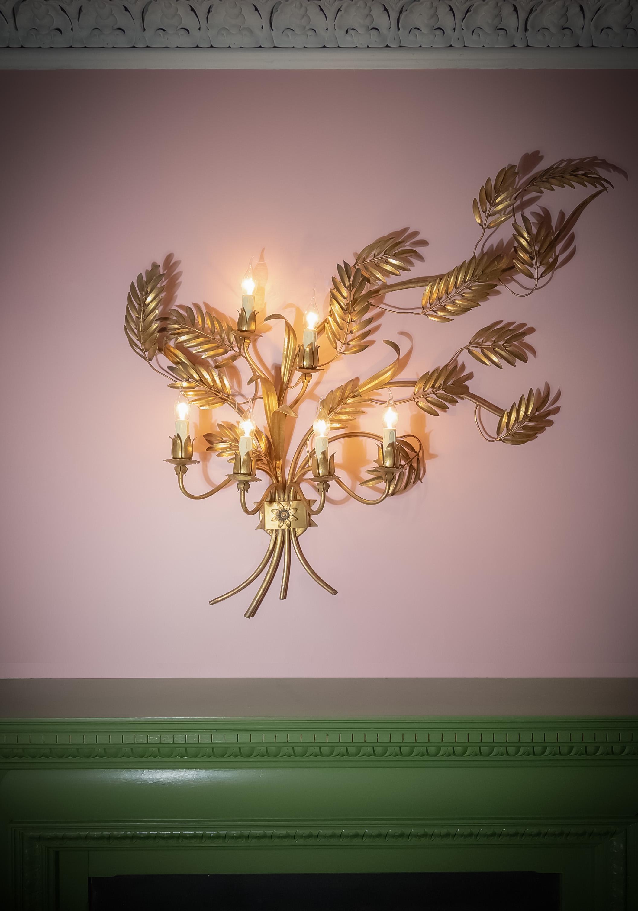 Grande applique murale Toleware en métal doré, fabriquée en Italie dans les années 1960, reflétant le glamour audacieux du design Hollywood Regency. 

La composition sculpturale prend la forme d'un arrangement de type gerbe de blé, avec des feuilles