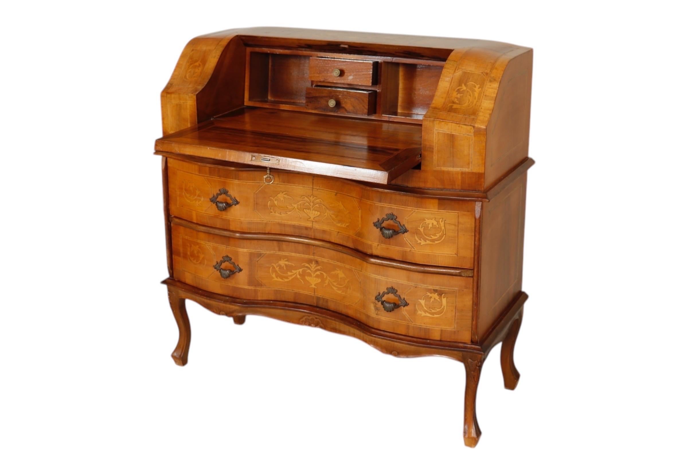 An Italian inlaid Venetian-style secretaire, circa 1960. Decorated throughout with walnut veneers, the drop front desk and two serpentine drawers are inlaid with satinwood marquetry urns and scrolled acanthus. The writing desk locks with the