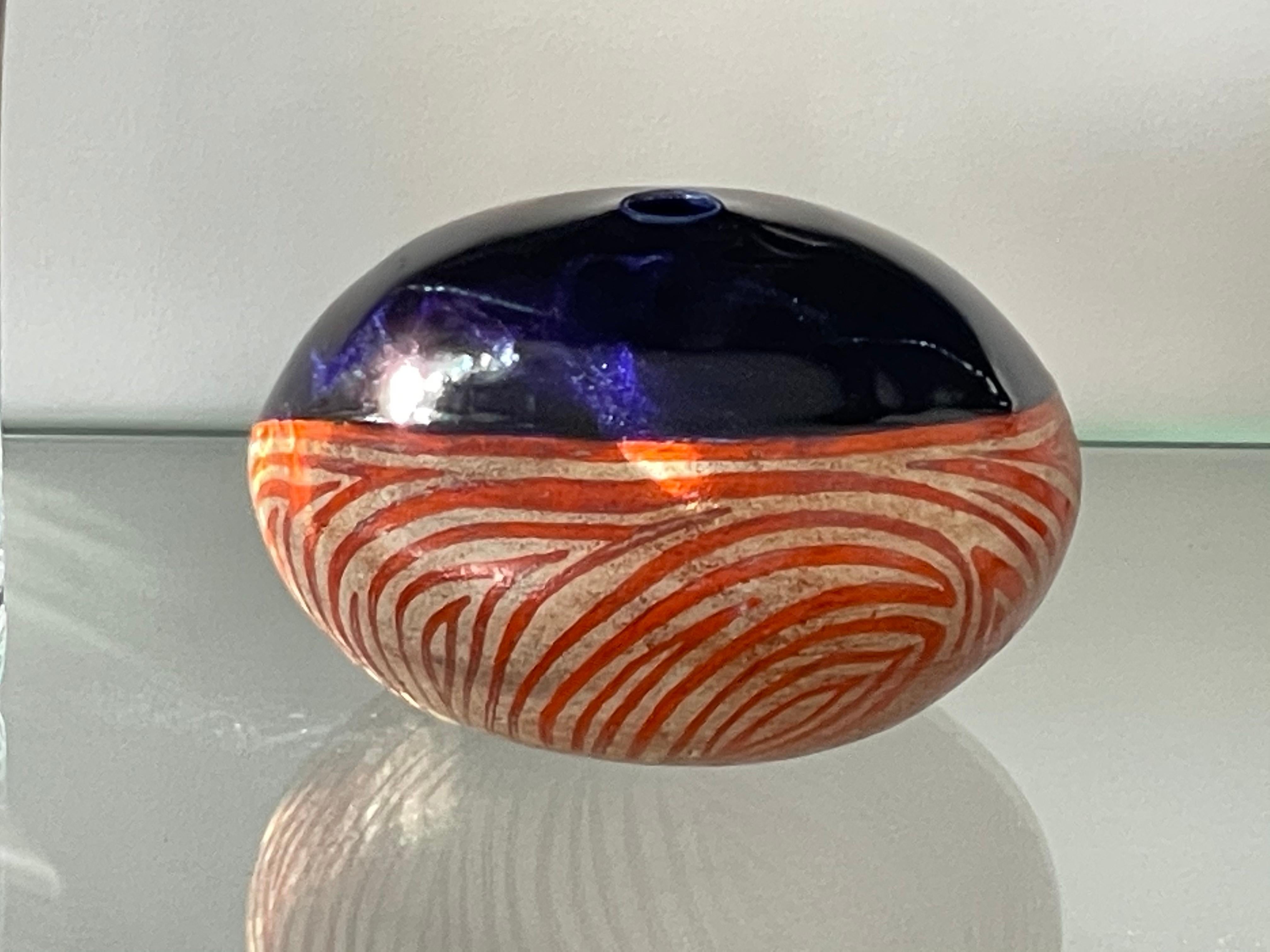 Italian 20th-century vintage circular or boule-shaped ceramic vase signed L Poli is highlighted by contrasting colors and patterns: dark blue at the top half and spiraling orange and white handpainted stripes at the bottoms. 
Italy. Circa 1960's