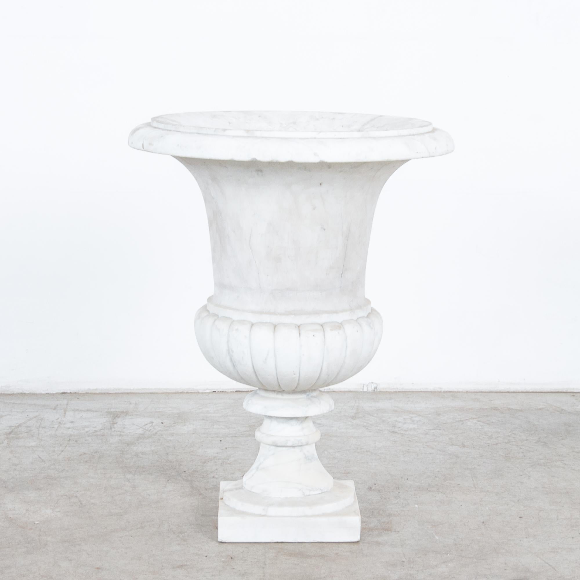 A campana style urn from 1960s Italy. A neoclassical silhouette which evokes the landscape gardens of sun-soaked Italian villas, rendered in white marble, veined with grey. A flared lip blossoms into an upturned bell-shape; a small pedestal elevates