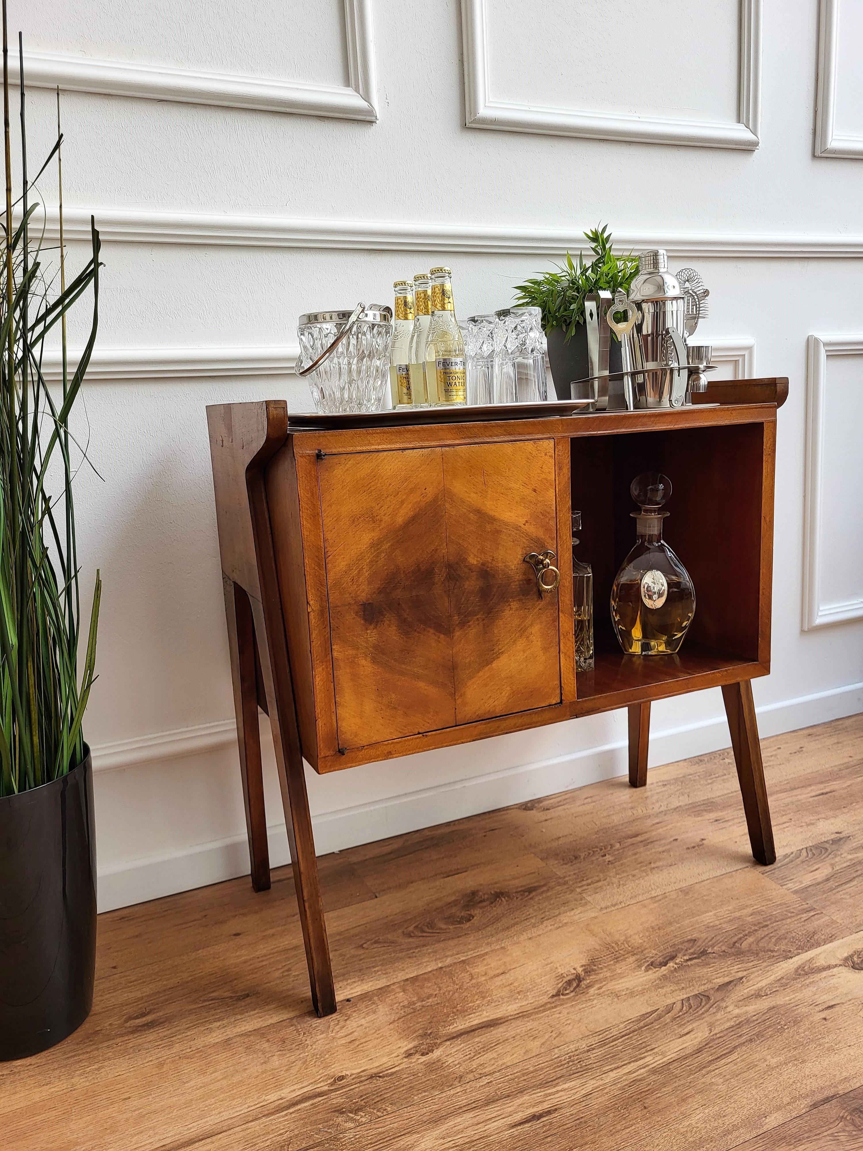 Beautiful and very elegantly shaped Italian Mid-Century Modern dry bar cabinet, with highlighted wood grain and brass handles. The left door opens to a nice storage space and the cabinet is standing on its greatly shaped 4 legs in the immediately