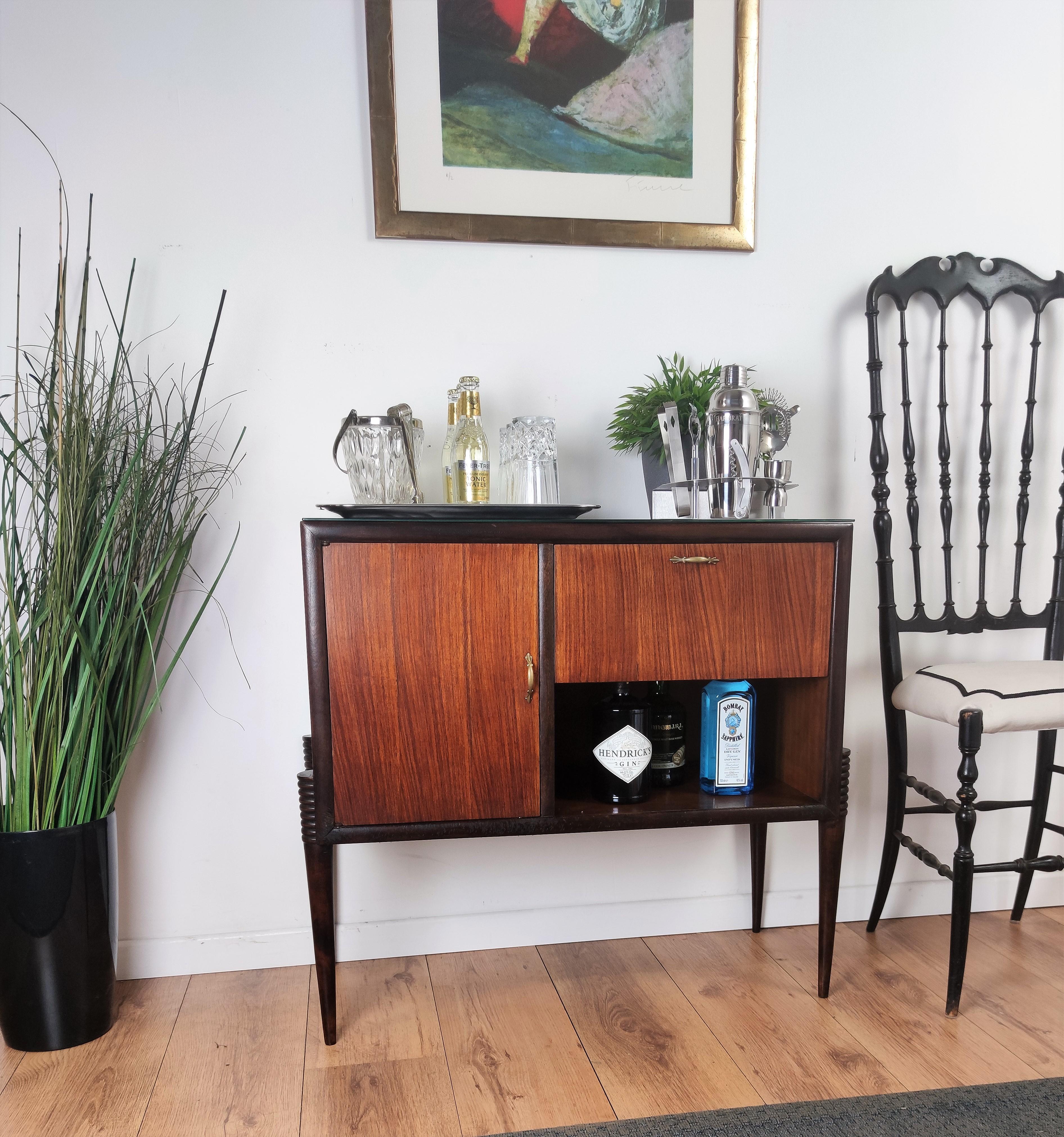 Beautiful and very elegantly shaped Italian Mid-Century Modern dry bar cabinet, with highlighted wood grain, black frame and great attention to details such as the brass handles and the black glass top. The left door opens to a nice storage space