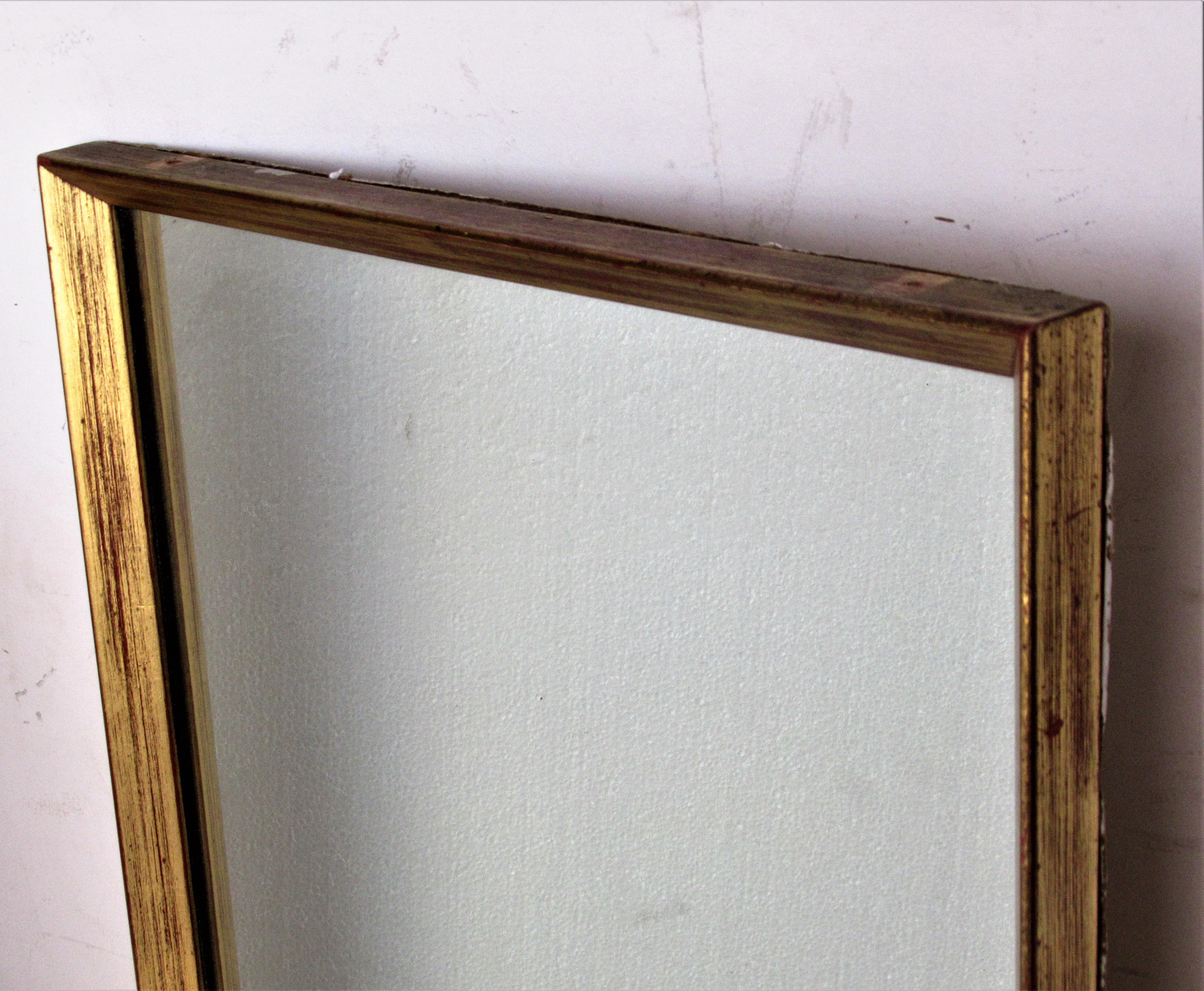 Mid-Century Modern long rectangular giltwood framed mirror with a simple elegant design in overall beautifully aged gilded surface showing areas of underlying red bole. Most likely Italian in origin, circa 1960. Look at all pictures and read