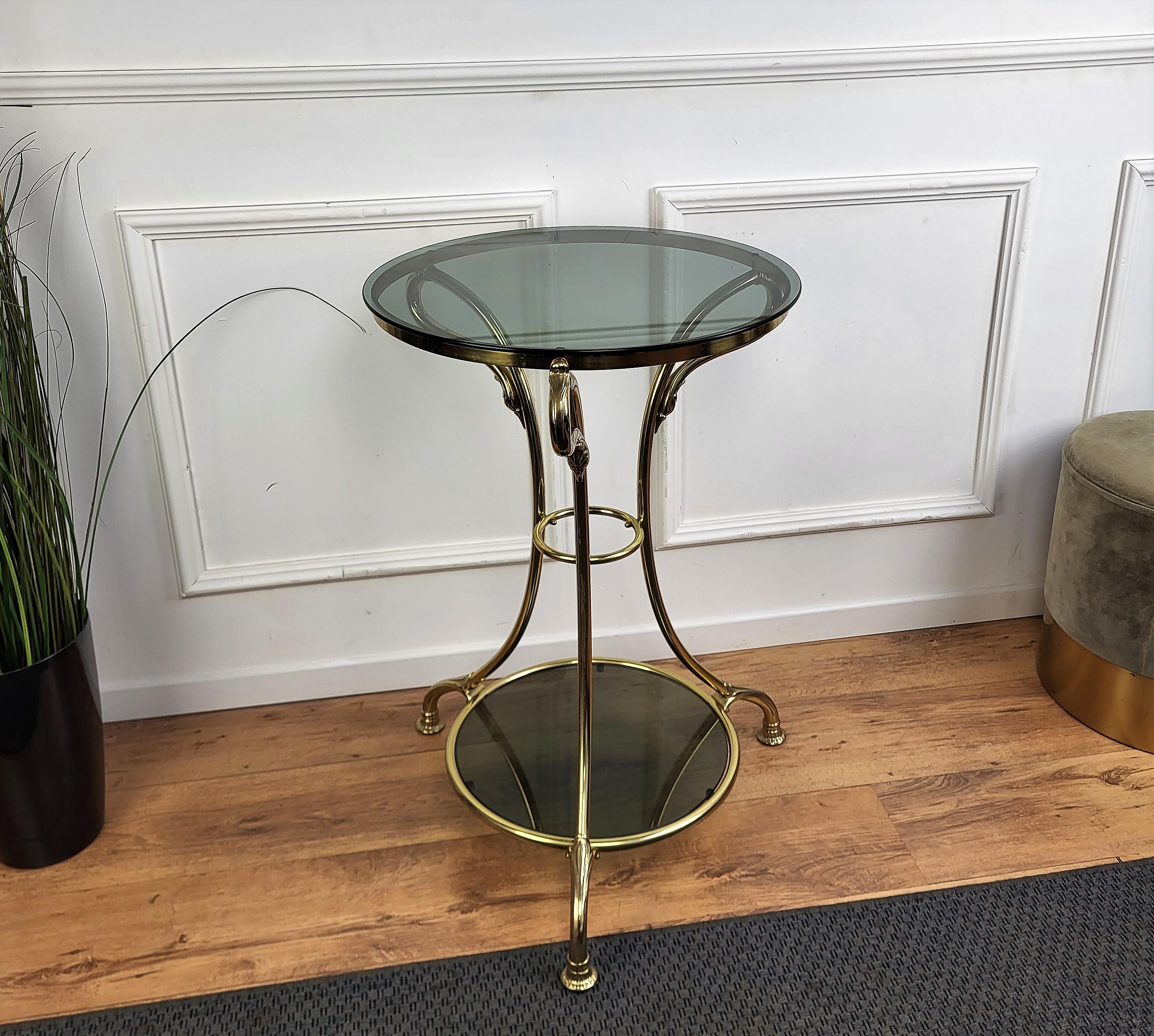 Beautiful and stylish vintage 1980s Italian brass and smoked glass gueridon side table or coffee table or sofa table. Very good condition with the main brass structure decorated and shaped with three swan heads and 2 round dark glasses. 
A great
