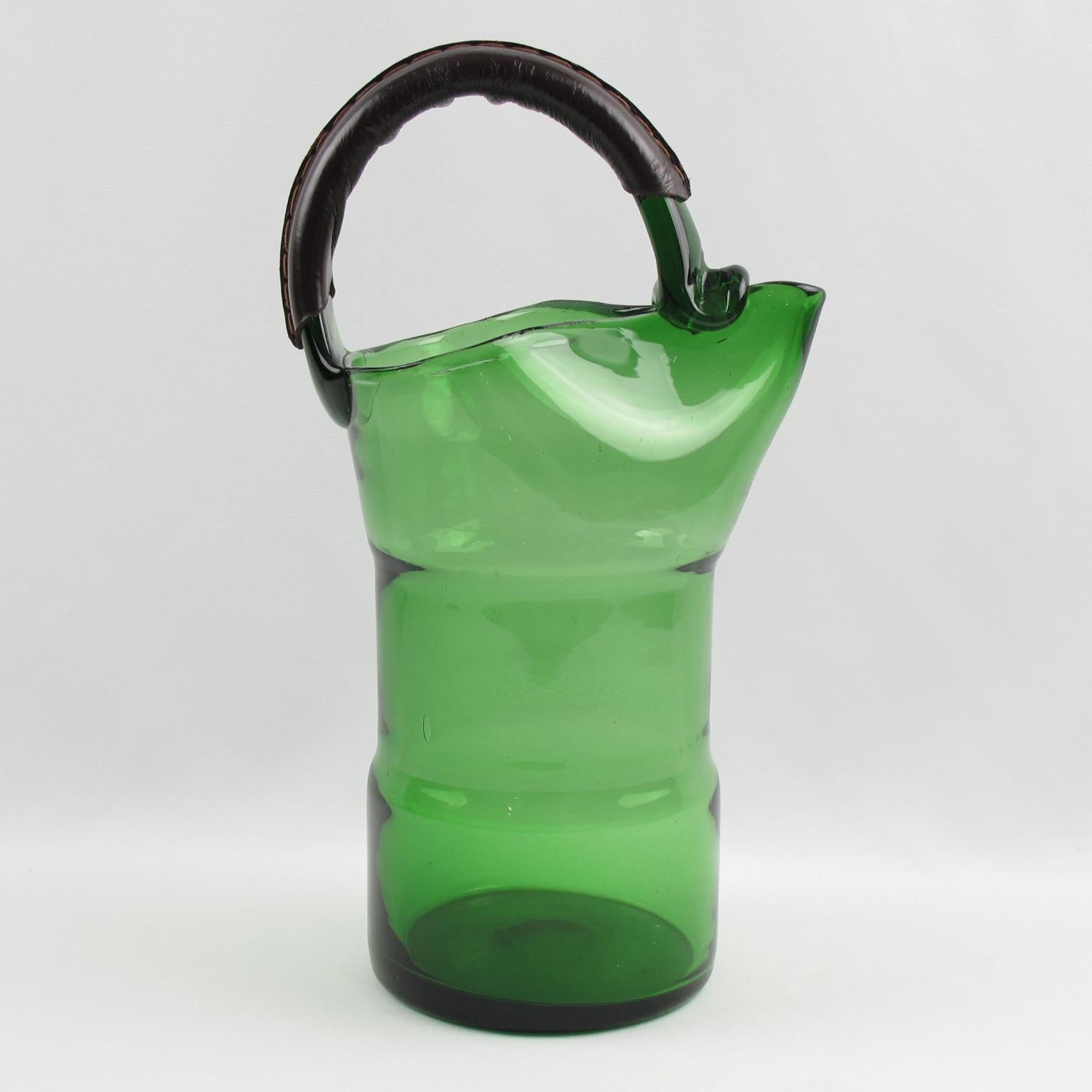 Stunning 1960s modernist Italian mouth-blown glass pitcher. Perfect for barware use and to serve lemonade or water, this lovely green glass pitcher is accented with a very unusual dark brown hand-stitched leather handle. Polished pontil mark on the