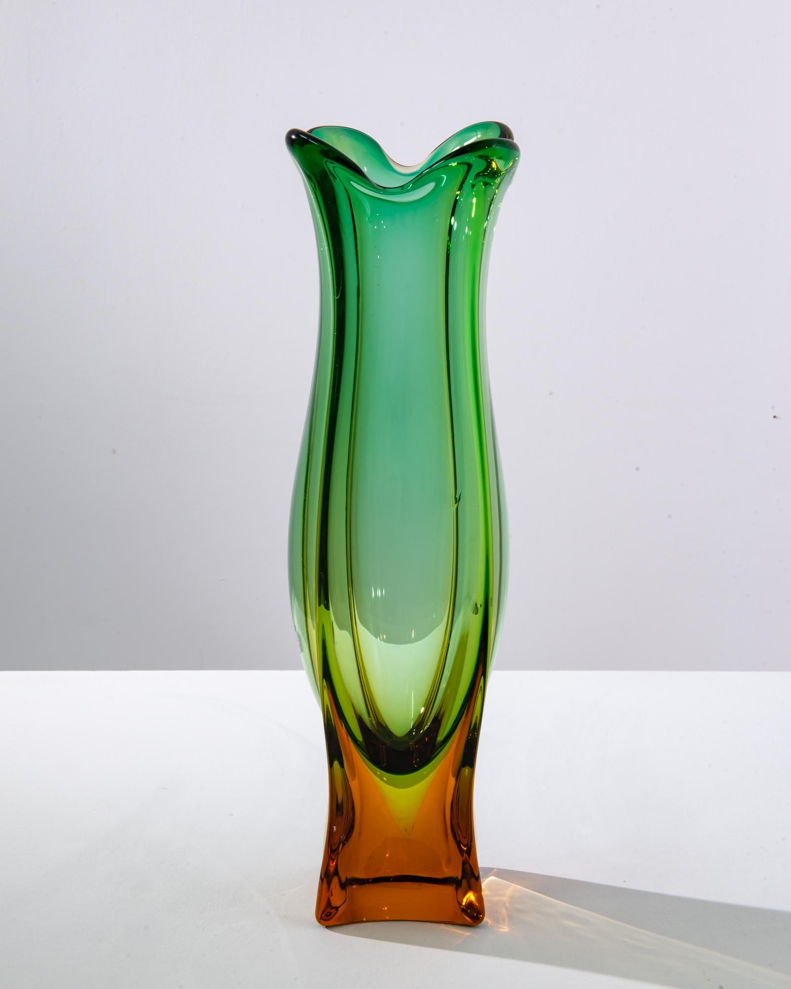 A glass vase made in 1960s Italy. This dazzling vase was made by Murano Glass, a renowned manufacturer from Venetia, a region famous for thousands of years of artisanal glassblowing. Orange-yellow hues ascend towards a bulbous body of the vessel,