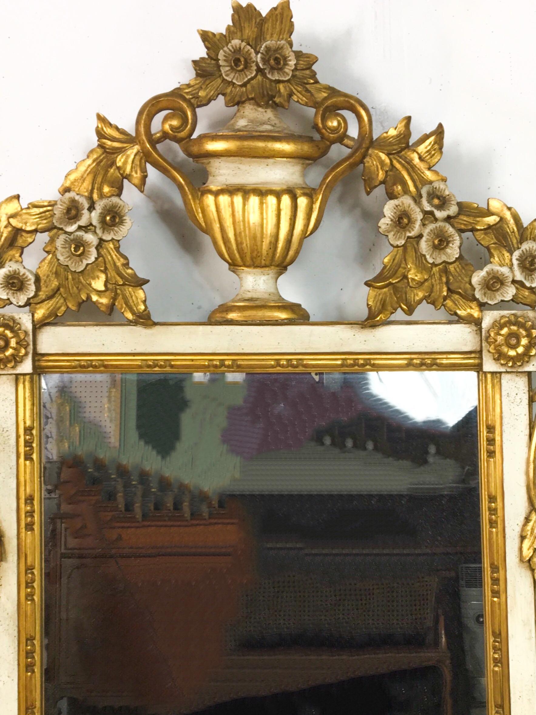 This is a lovely 1960s Italian neo-classical style carved giltwood floral and urn motif mirror. It is both ivory paint and gilt. It is in very good condition.