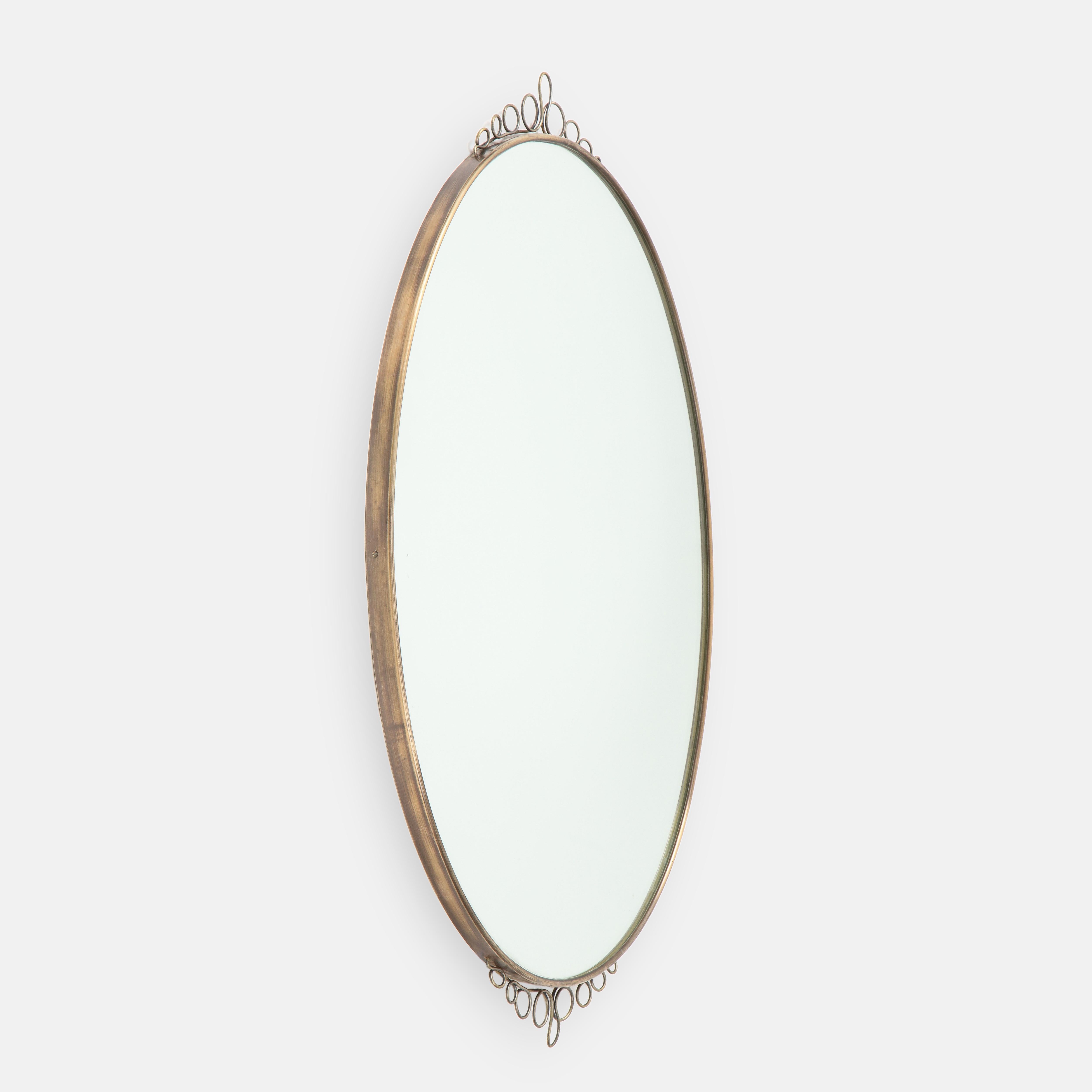 Elegant oval brass wall mirror with lovely decorative brass element on central top and bottom, Italy, 1960s. This charming midcentury mirror illustrates in its playful decorations Italian Novecento design characteristic of this period. The mirror