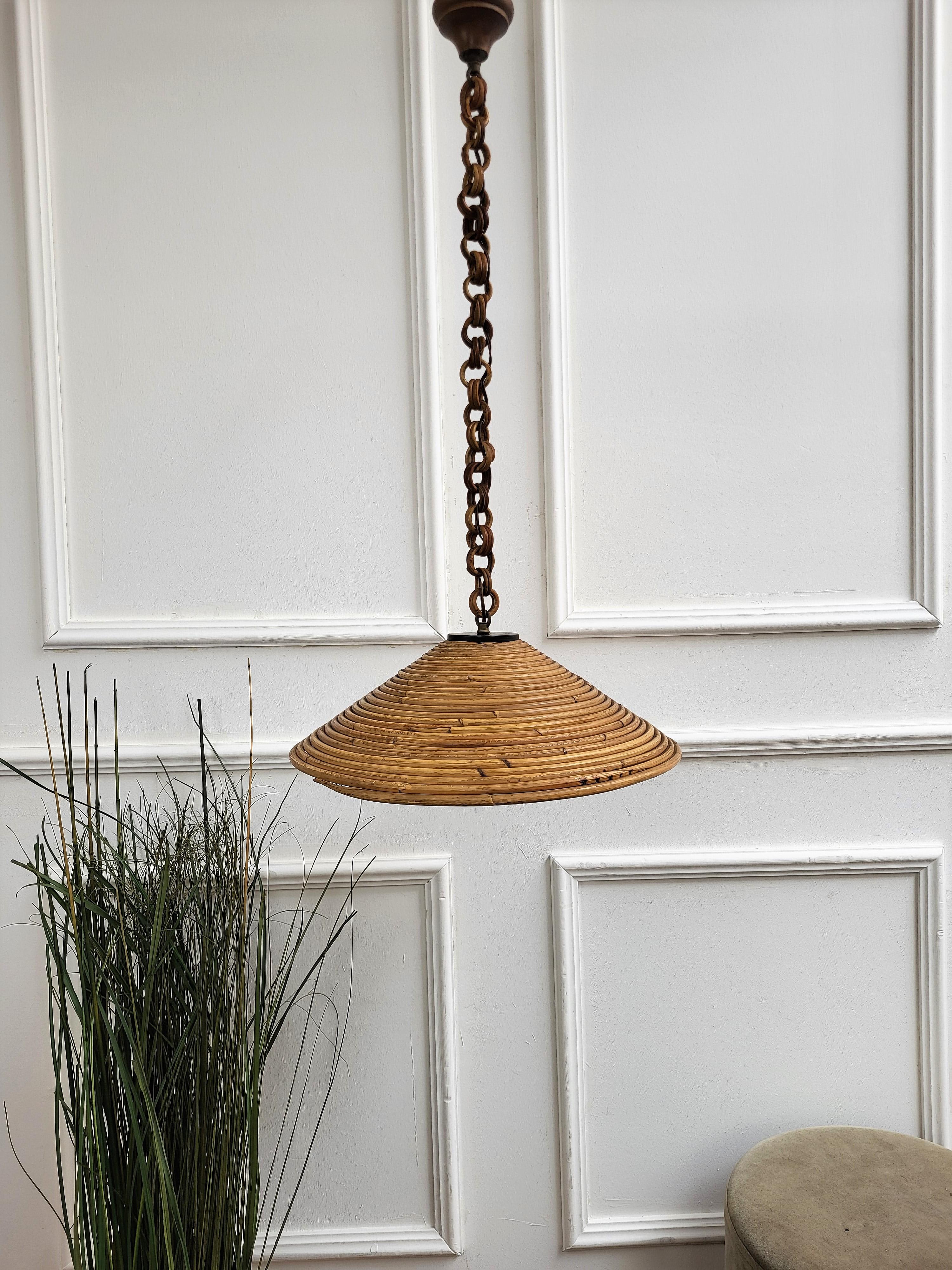 Eyecatching Italian 1960s handcrafted rattan pendant light with circular design. This suspension lamp has a bell shaped lampshade hanging from a rattan bamboo chain topped by a wooden carved bun. The length of the chain can be shortened removing