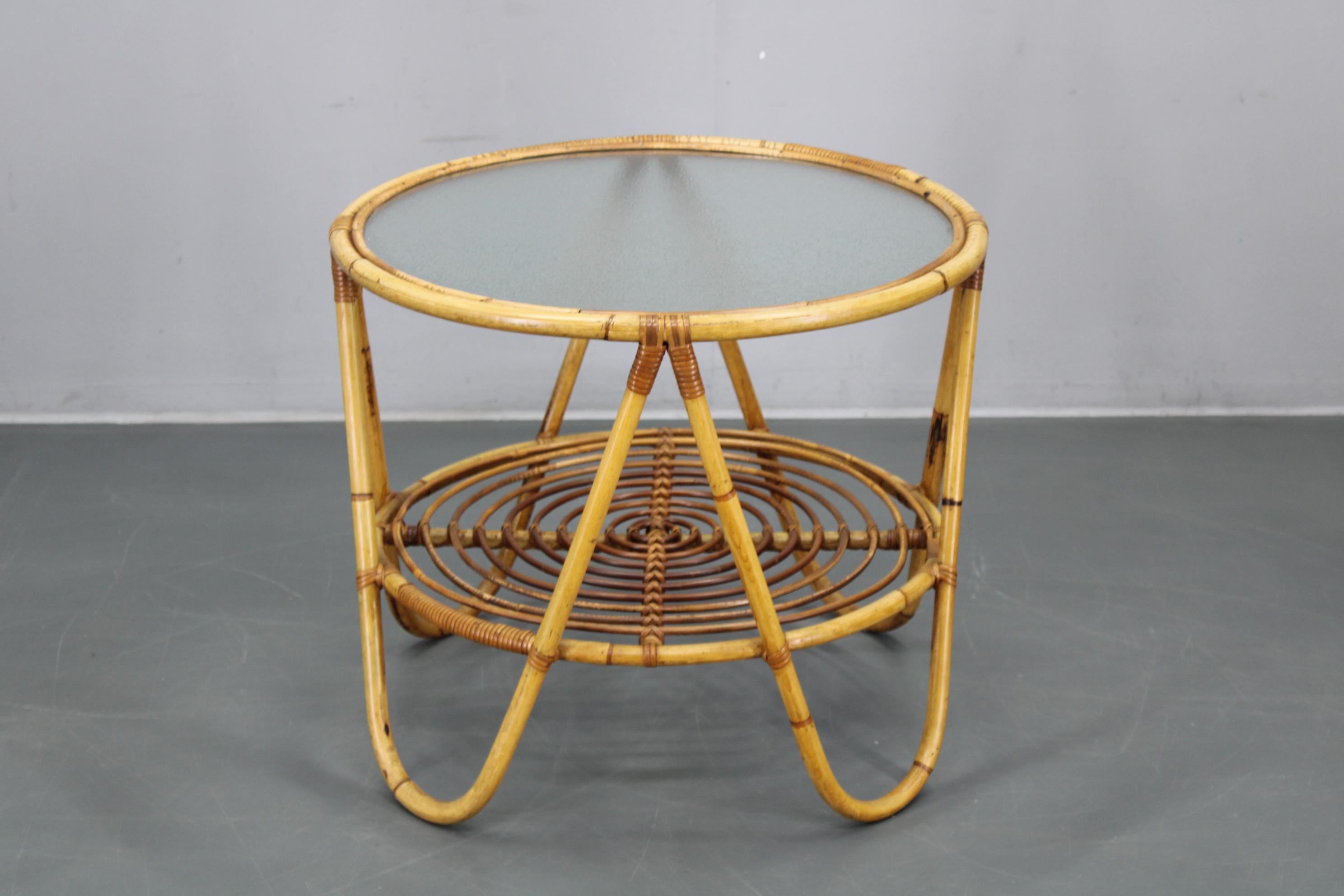 Cette élégante table basse en rotin italien des années 1960 présente un cadre rond tressé associé à un plateau en verre texturé, illustrant les courbes organiques et le savoir-faire artisanal caractéristiques du design italien du milieu du siècle.