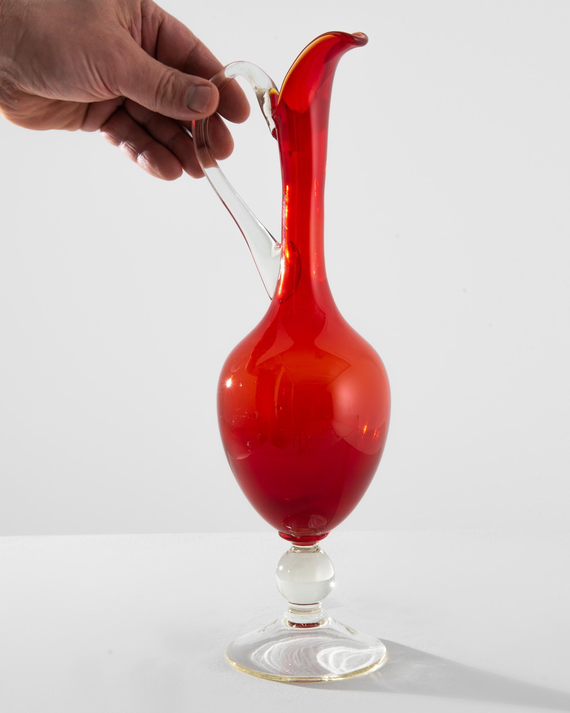 Introducing the quintessence of Italian elegance from the 1960s, this exquisite red glass jug is a testament to timeless design and artisanal craftsmanship. With its vibrant ruby hue that captures the light, creating a warm, inviting glow, this jug
