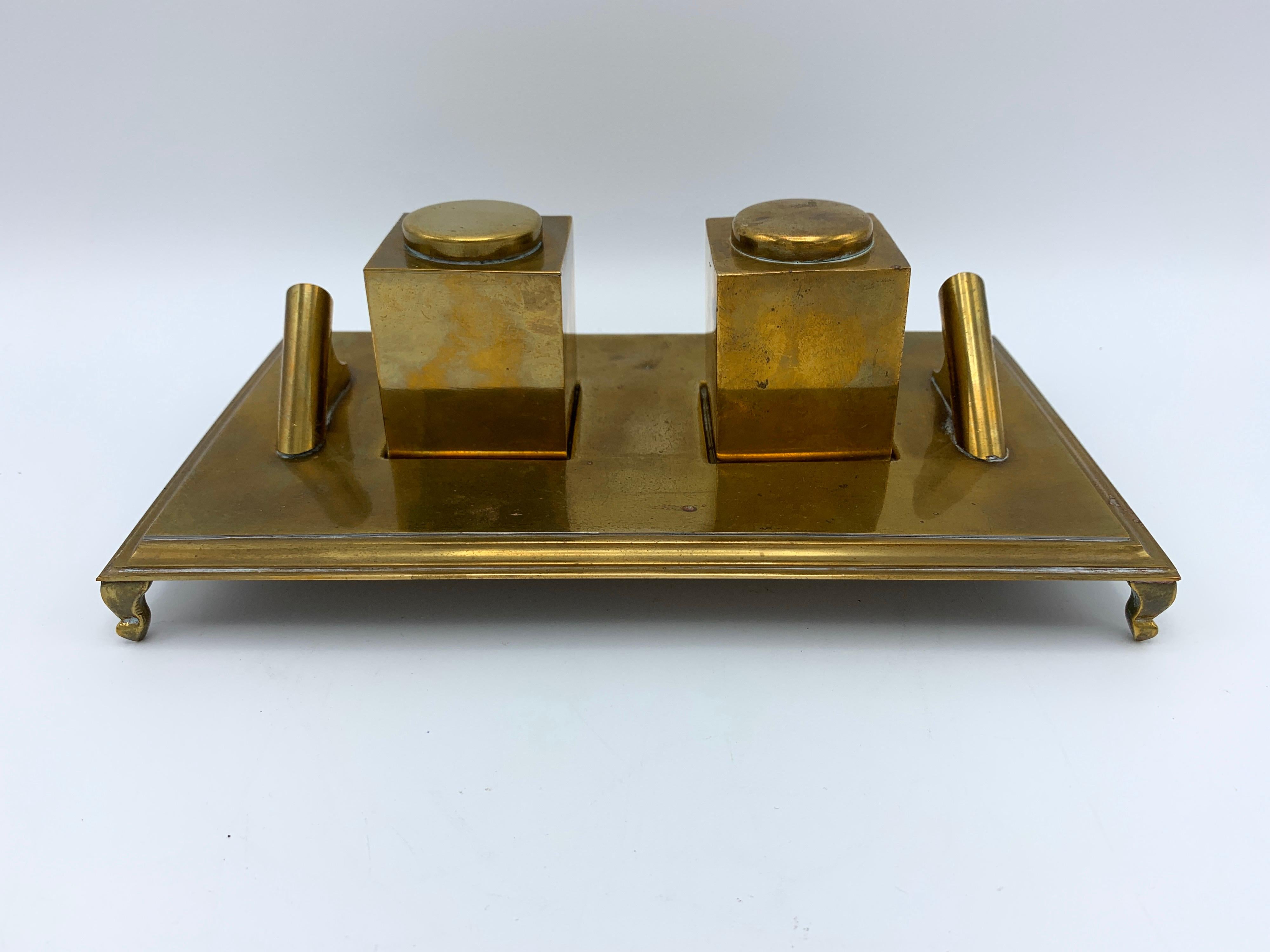 Listed is a gorgeous, 1960s Italian brass inkwell desk set, by Sarreid Ltd. This desk set includes two 'inkwells' (one is a functioning inkwell with removable cap, the second is a paperweight without a removable cap) and a footed tray, featuring two