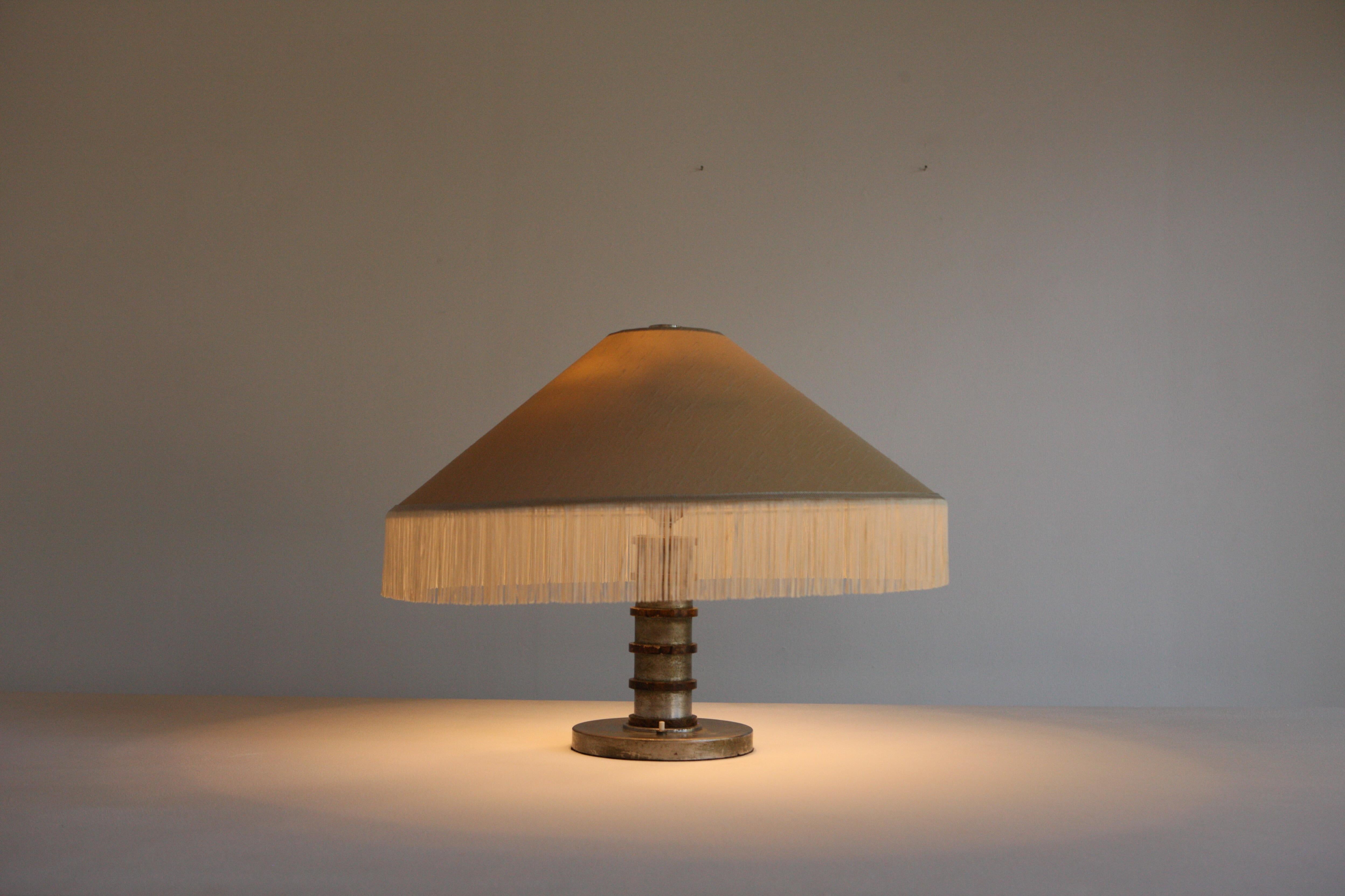 A large 1940's metal table lamp with a stacked cylindrical steel base and enamelled orb detail. We have had this Italian lamp rewired and the oyster silk shade restored to its original fringed splendour. A beauty.