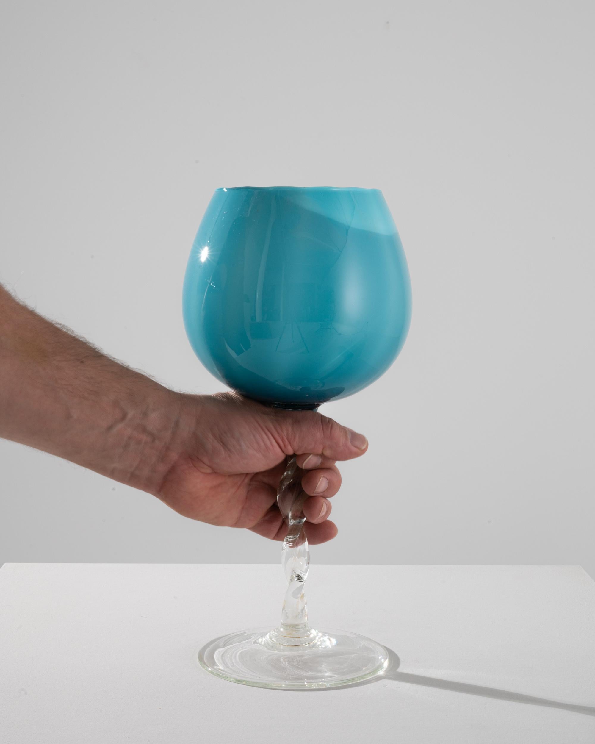 Indulge in the essence of retro luxury with this captivating Italian Teal Glass Goblet from the 1960s, a piece that promises to add an air of sophistication to any table setting. The goblet features a bold, balloon-shaped bowl, which beautifully