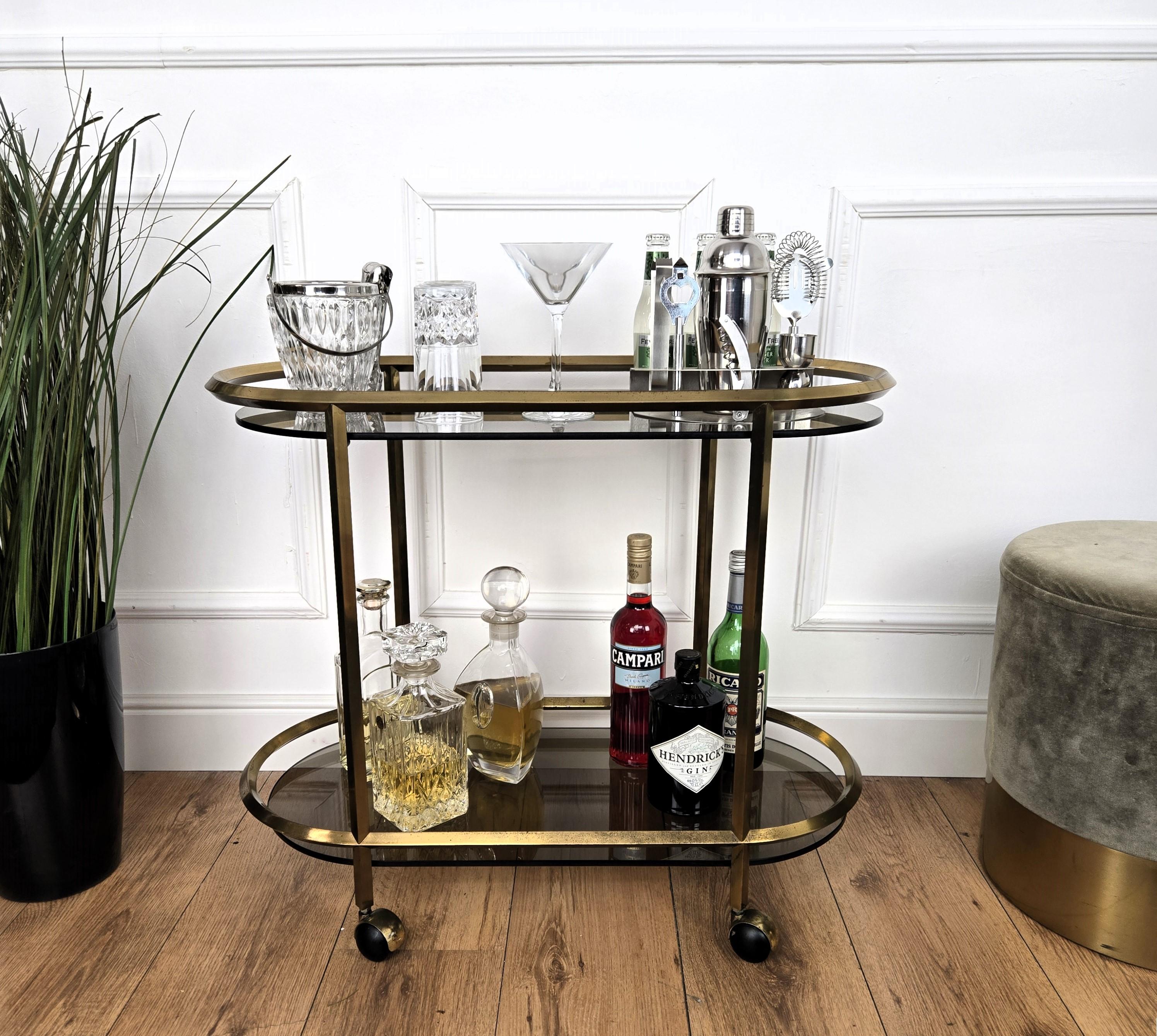 Magnifique et élégant chariot de bar à deux niveaux en laiton et verre fumé de style Hollywood Regency italien des années 1960. Une pièce exceptionnelle qui ajoute parfaitement à la décoration de chaque maison le faste, le glamour et l'or typiques